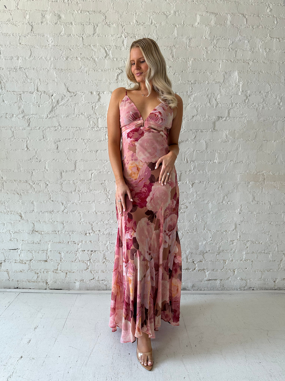 Woman wearing blush floral maxi dress with v-neckline and metal loop detailing. 