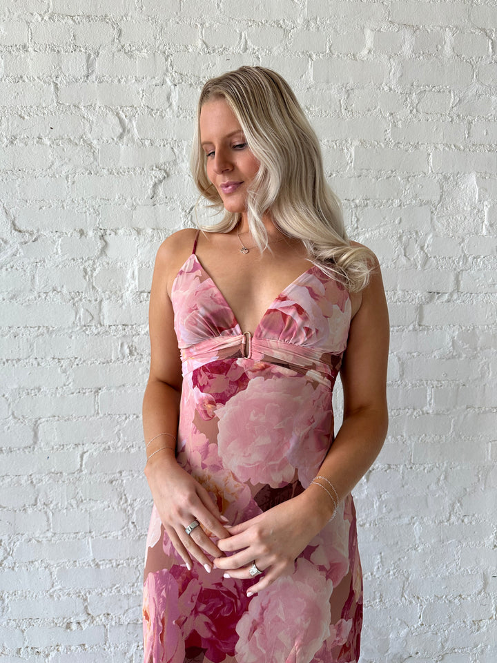 Woman wearing blush floral maxi dress with v-neckline and metal loop detailing. 