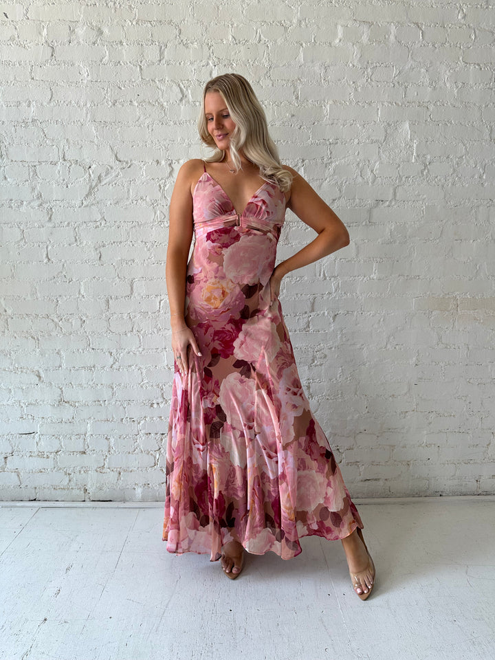 Woman wearing blush floral maxi dress with v-neckline and metal loop detailing. 
