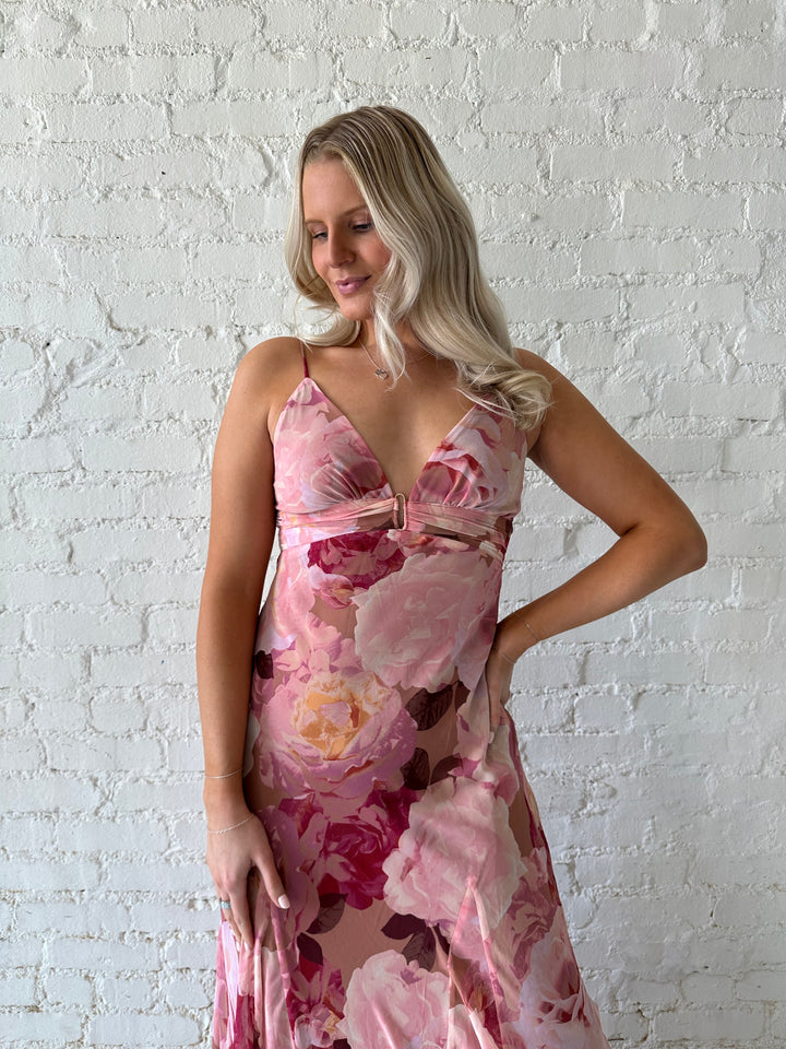 Woman wearing blush floral maxi dress with v-neckline and metal loop detailing. 