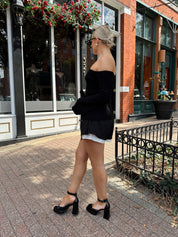 Woman wearing black ribbed off the shoulder top with belt tie detail.