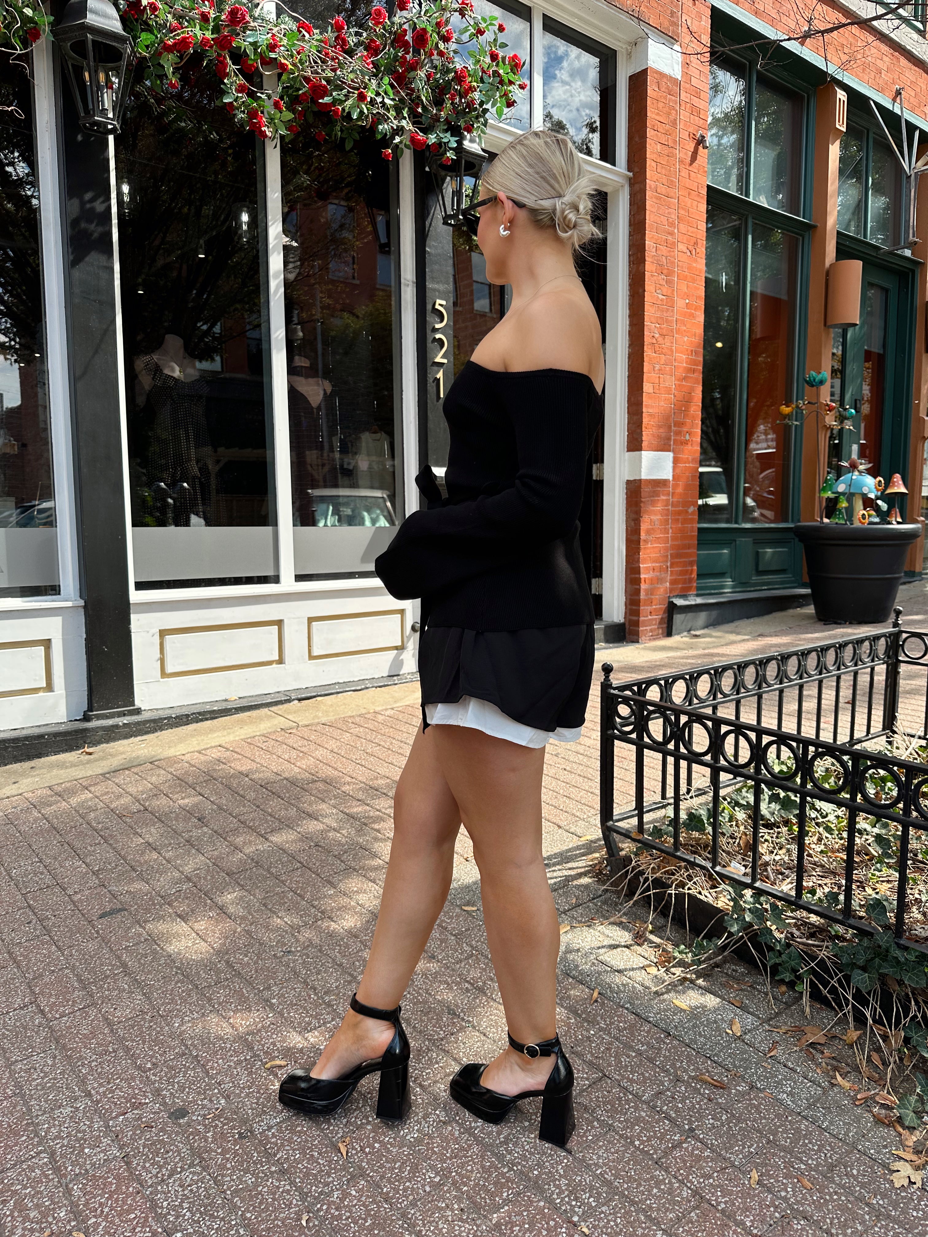 Woman wearing black ribbed off the shoulder top with belt tie detail.