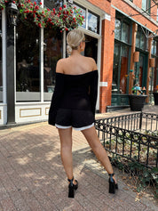 Woman wearing black ribbed off the shoulder top with belt tie detail.