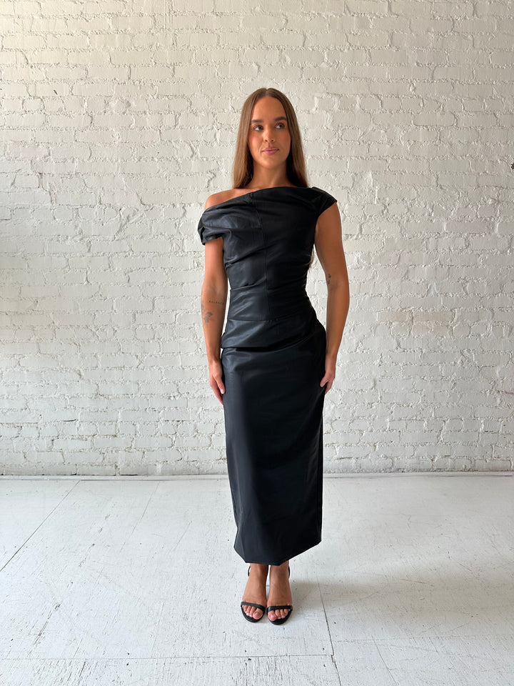 Woman wearing black leather midi dress with an asymmetrical neckline, and back slit.