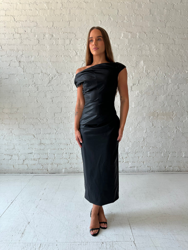 Woman wearing black leather midi dress with an asymmetrical neckline, and back slit.
