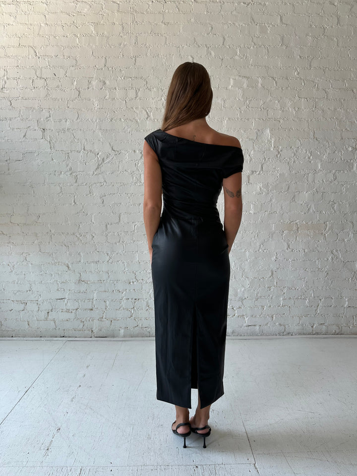 Woman wearing black leather midi dress with an asymmetrical neckline, and back slit.