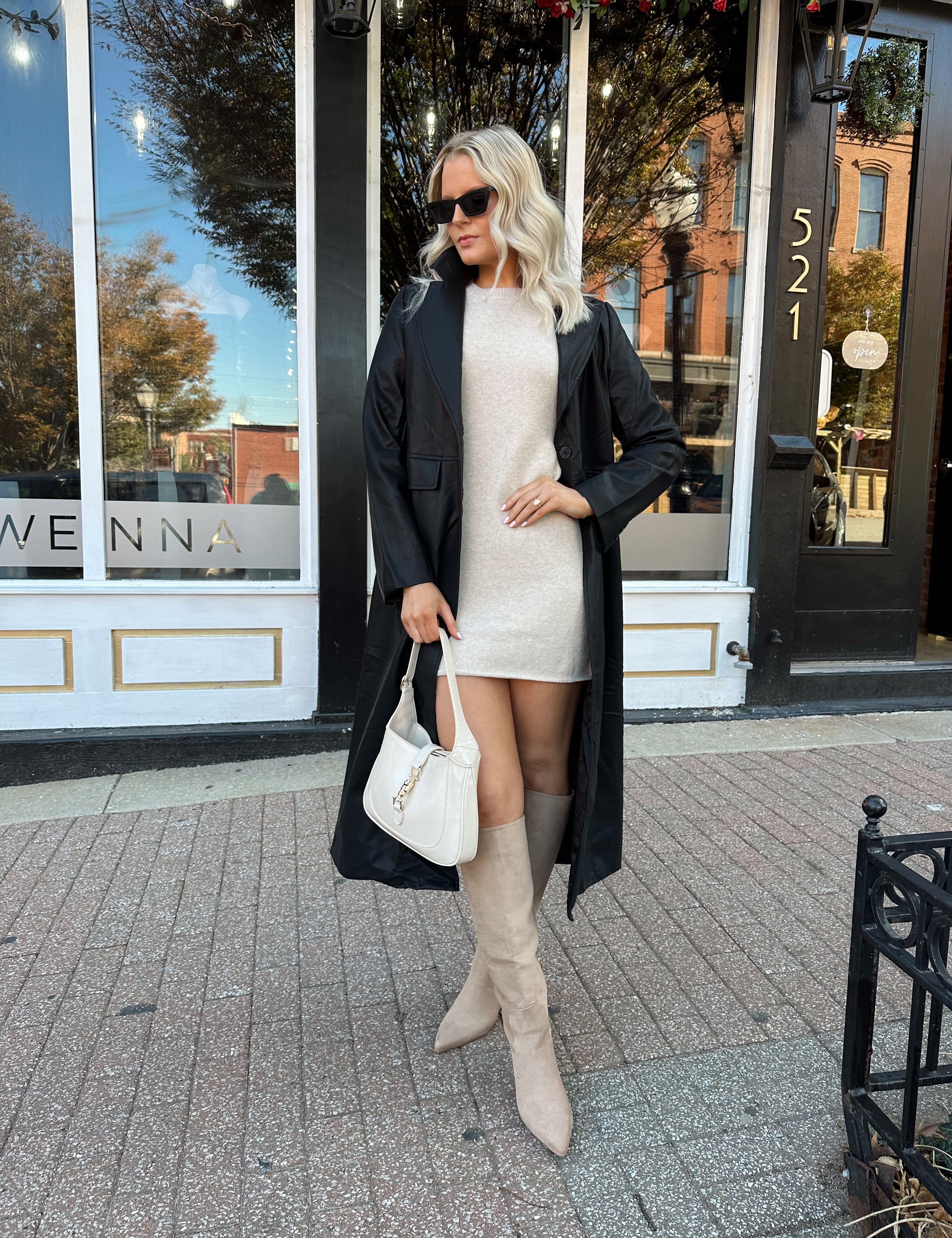 Woman wearing oatmeal knit short sleeve sweater dress and black trench coat.