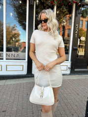 Woman wearing oatmeal knit short sleeve sweater dress and black trench coat.