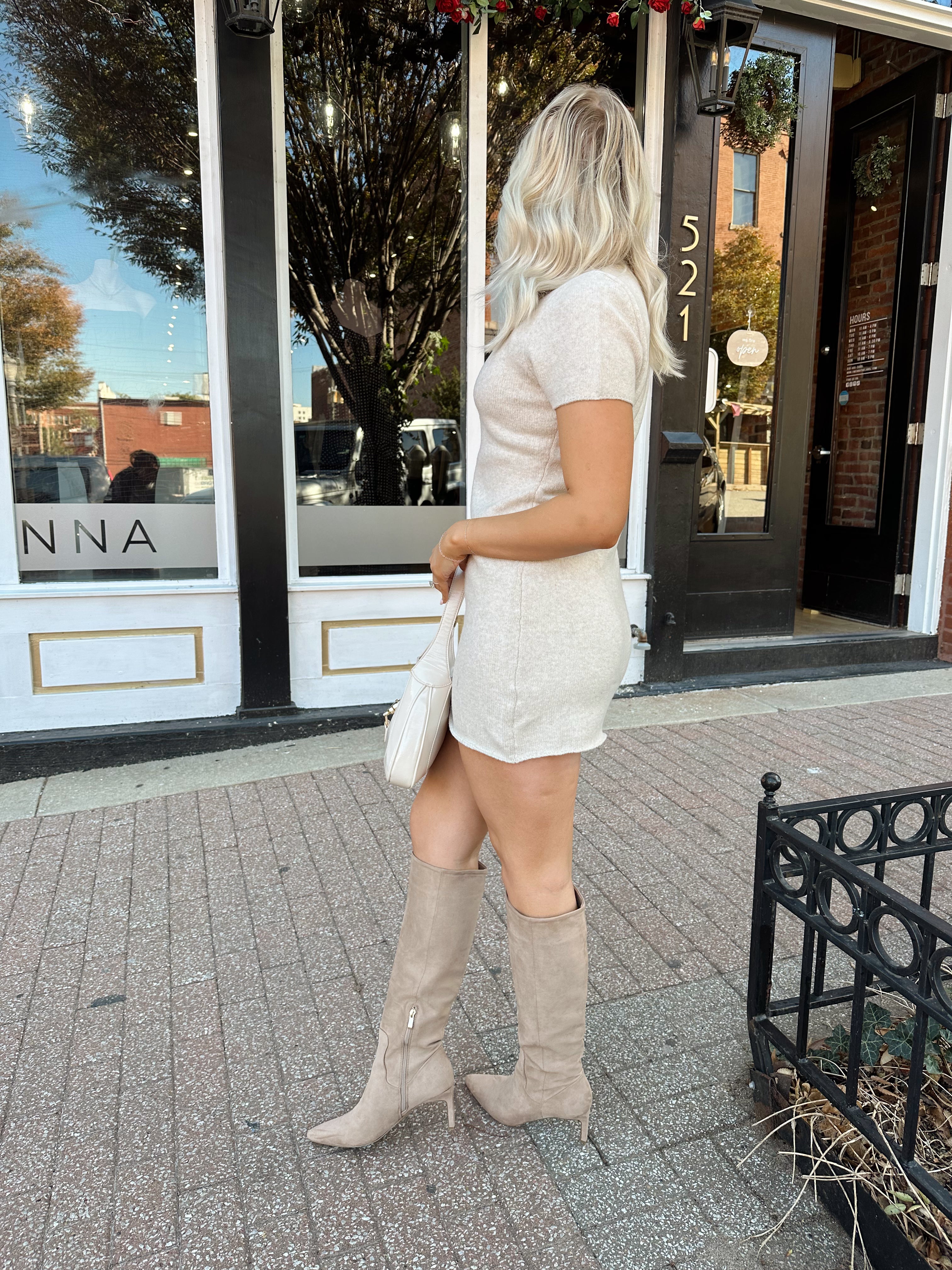 Woman wearing oatmeal knit short sleeve sweater dress and black trench coat.