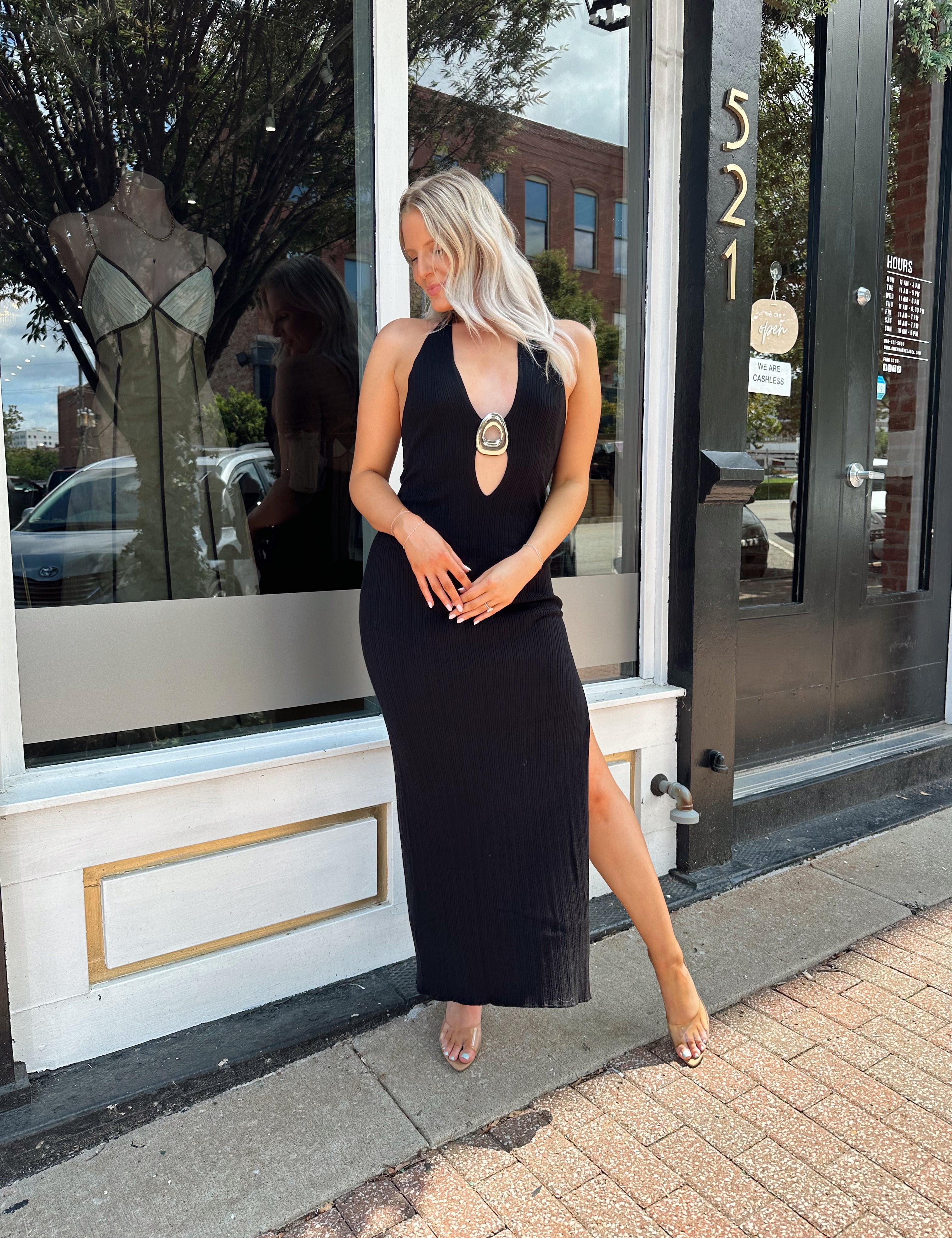 Woman wearing a black knit halter midi dress with keyhole stone cutout and side slit.
