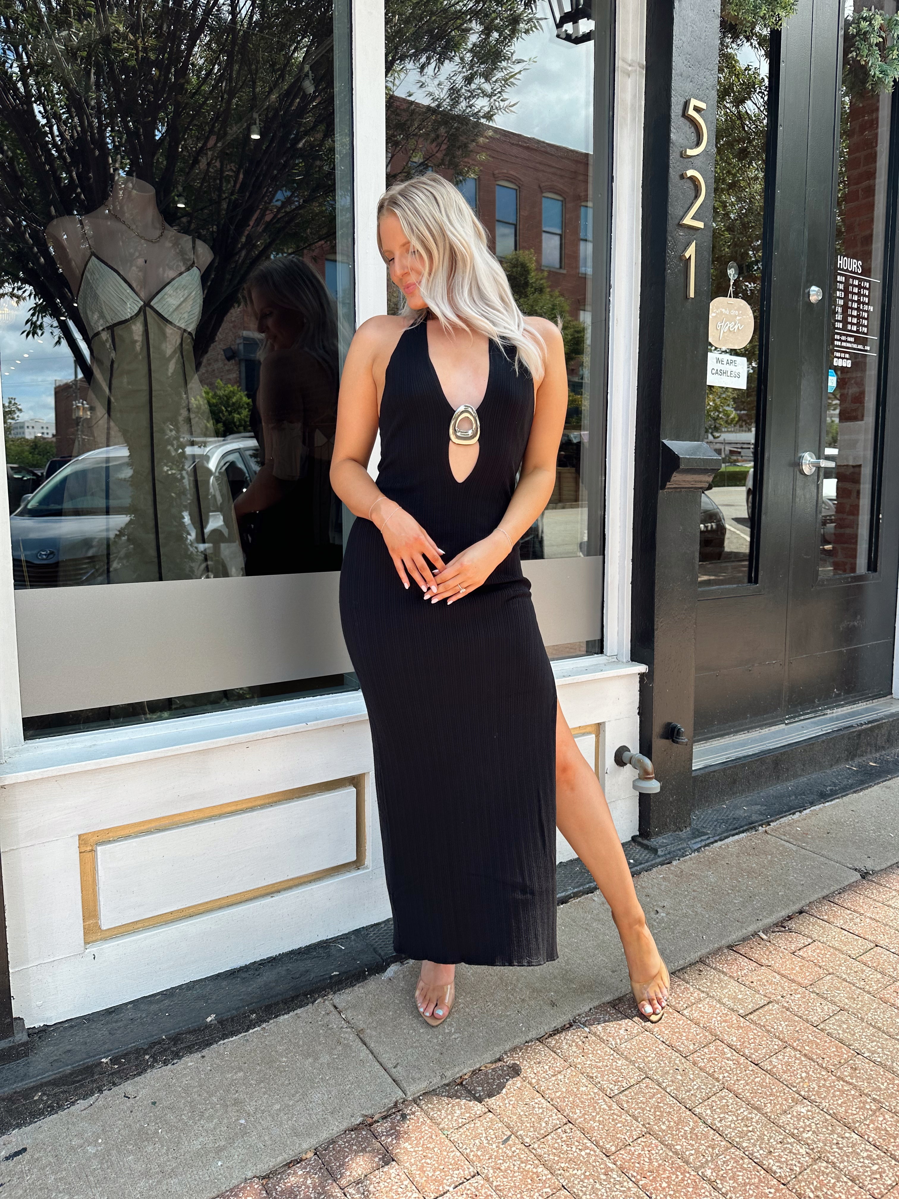 Woman wearing a black knit halter midi dress with keyhole stone cutout and side slit.