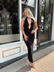Woman wearing a black knit halter midi dress with keyhole stone cutout and side slit.