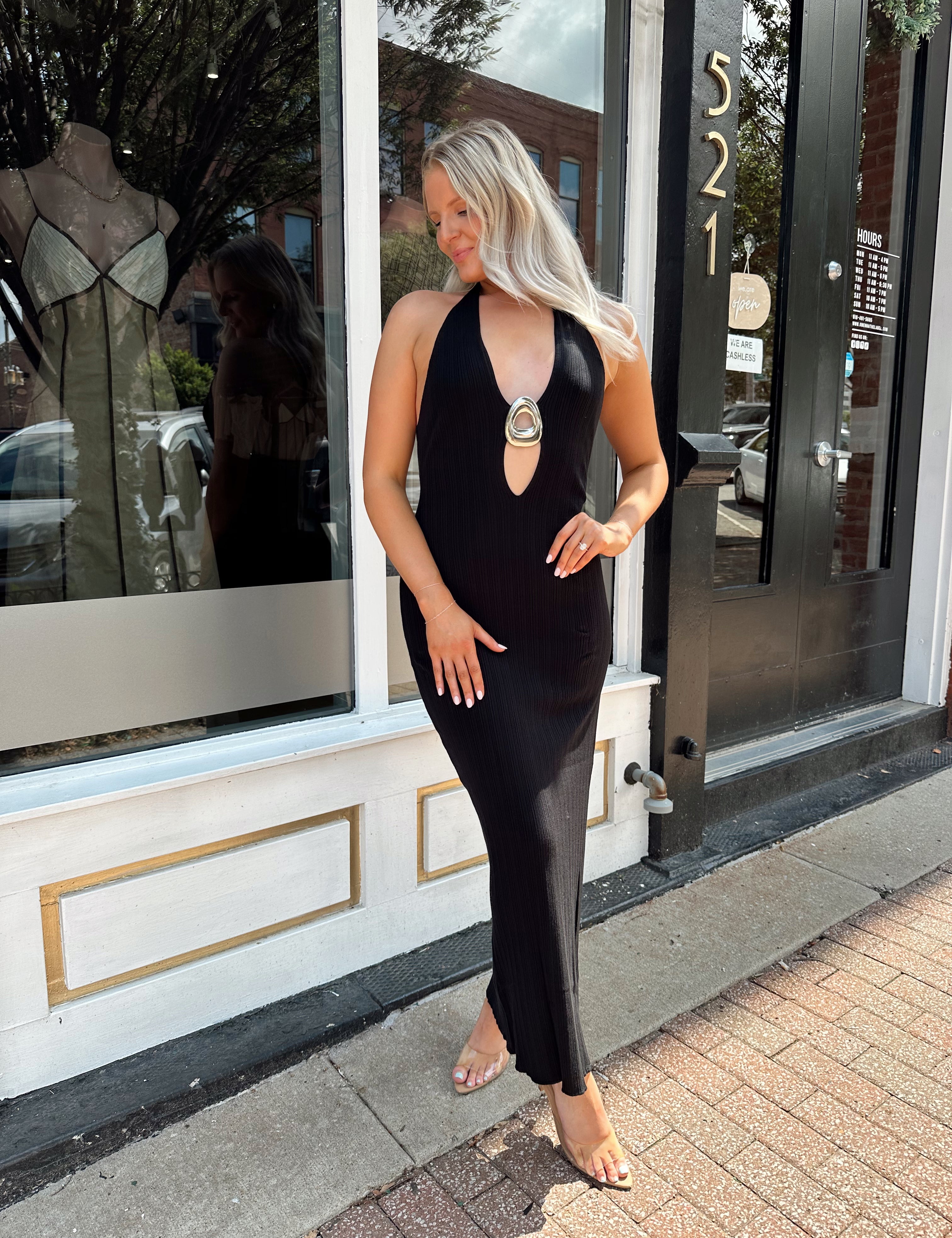 Woman wearing a black knit halter midi dress with keyhole stone cutout and side slit.