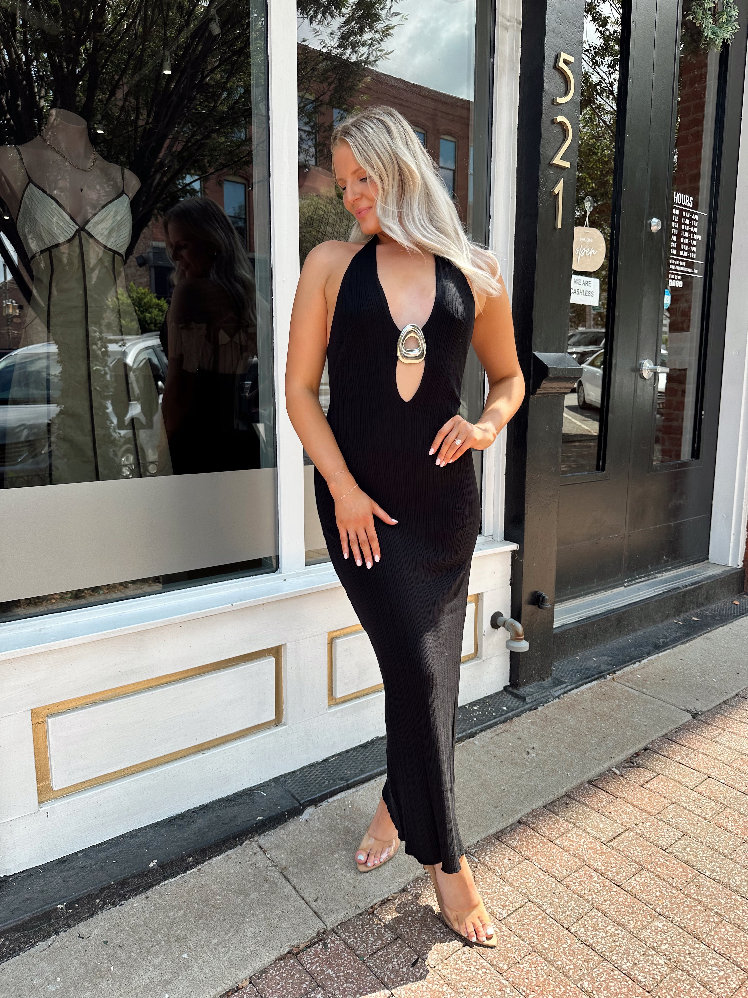 Woman wearing a black knit halter midi dress with keyhole stone cutout and side slit.