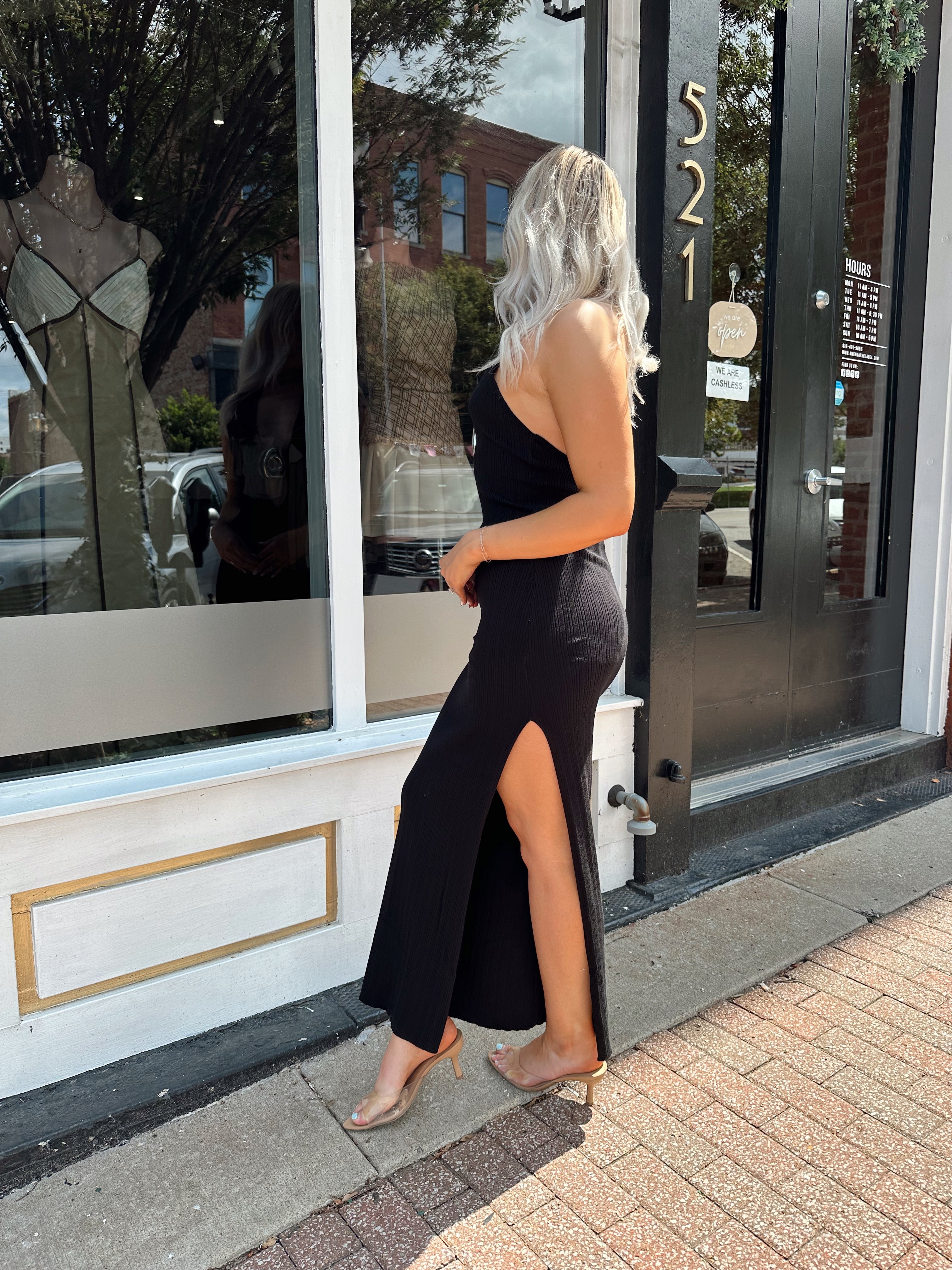 Woman wearing a black knit halter midi dress with keyhole stone cutout and side slit.