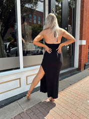 Woman wearing a black knit halter midi dress with keyhole stone cutout and side slit.