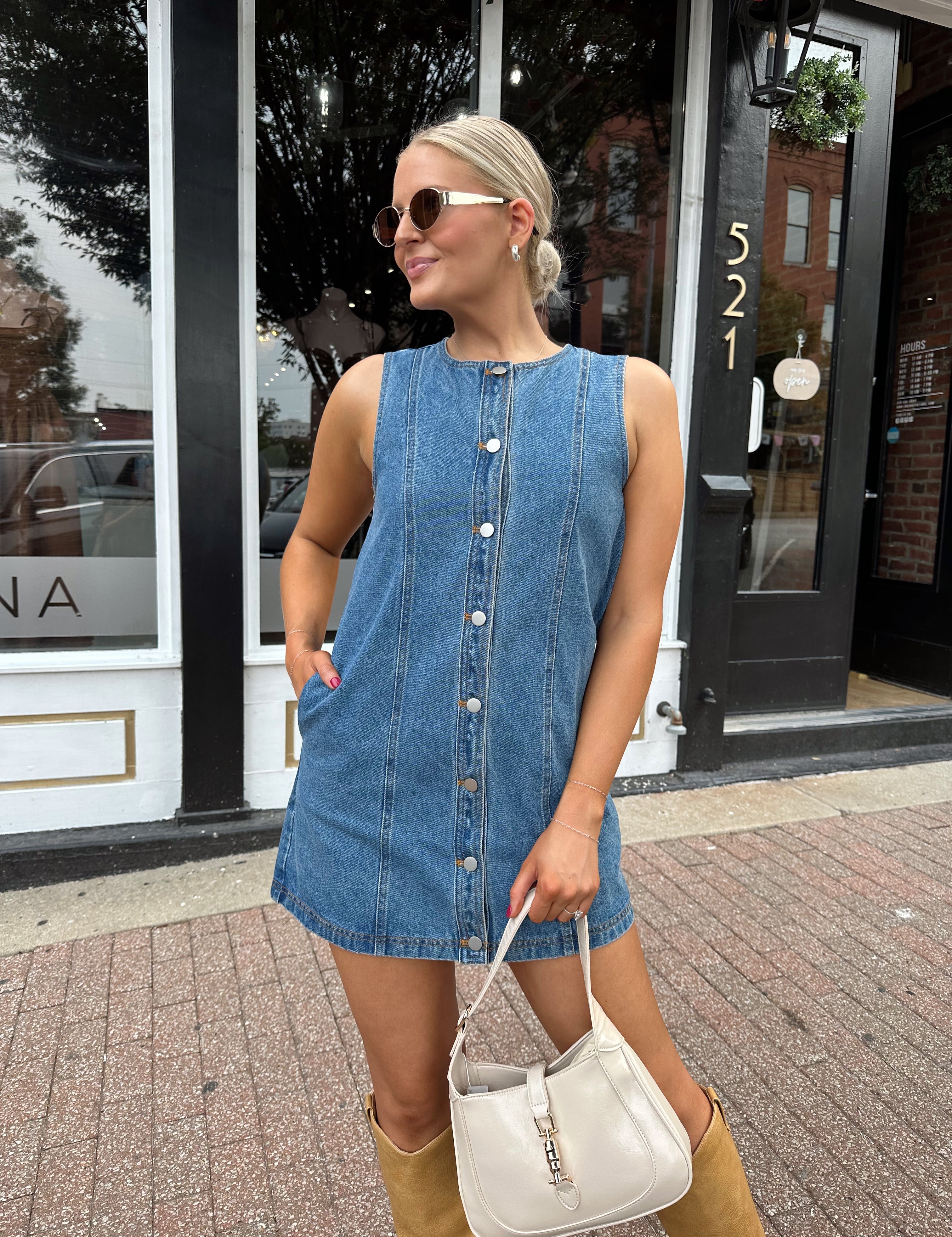 Woman wearing a medium wash denim mini dress with front button closure. 