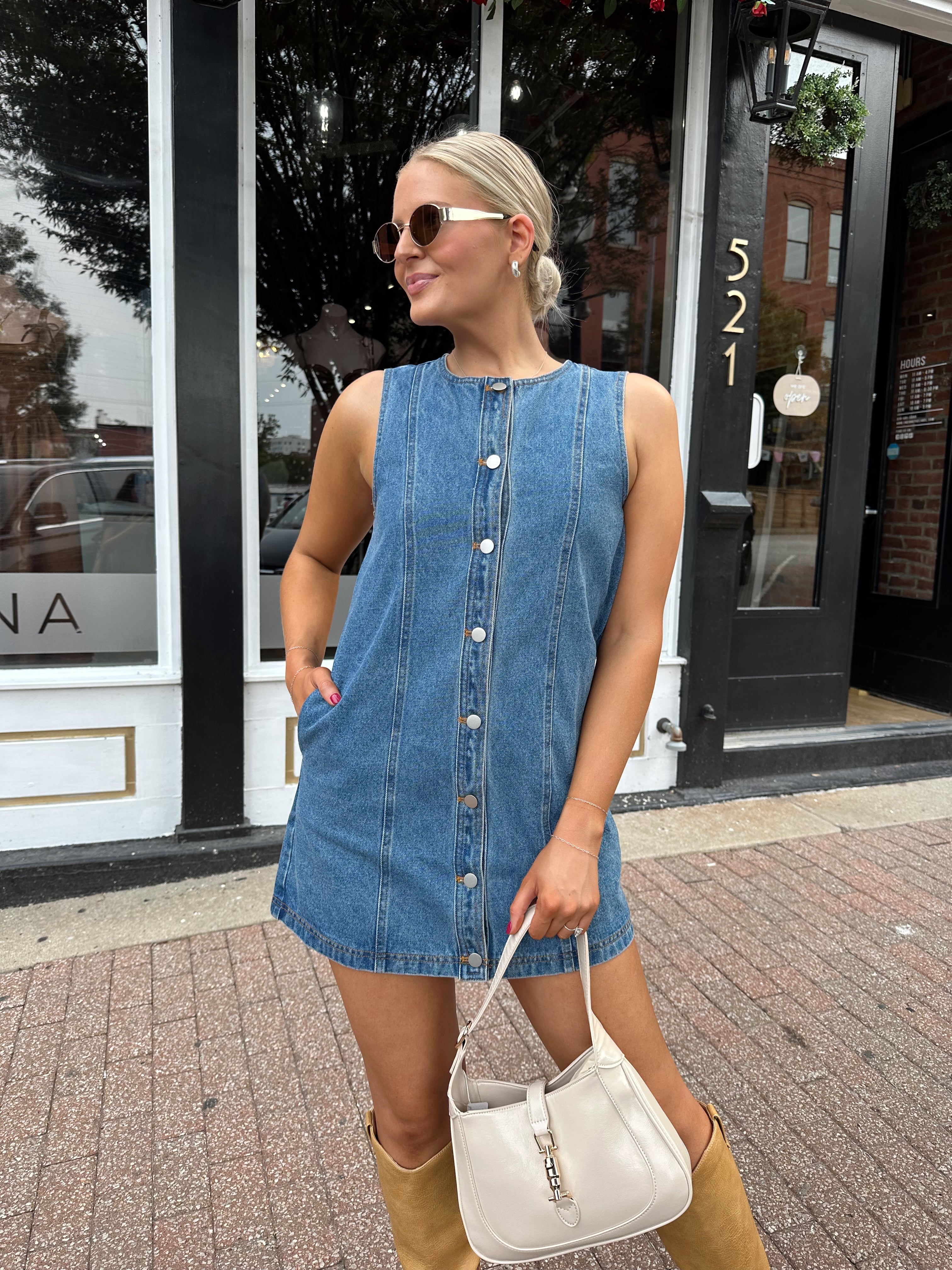 Woman wearing a medium wash denim mini dress with front button closure. 