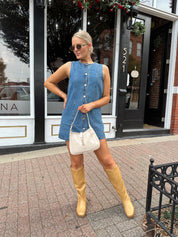 Woman wearing a medium wash denim mini dress with front button closure. 