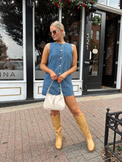 Woman wearing a medium wash denim mini dress with front button closure. 