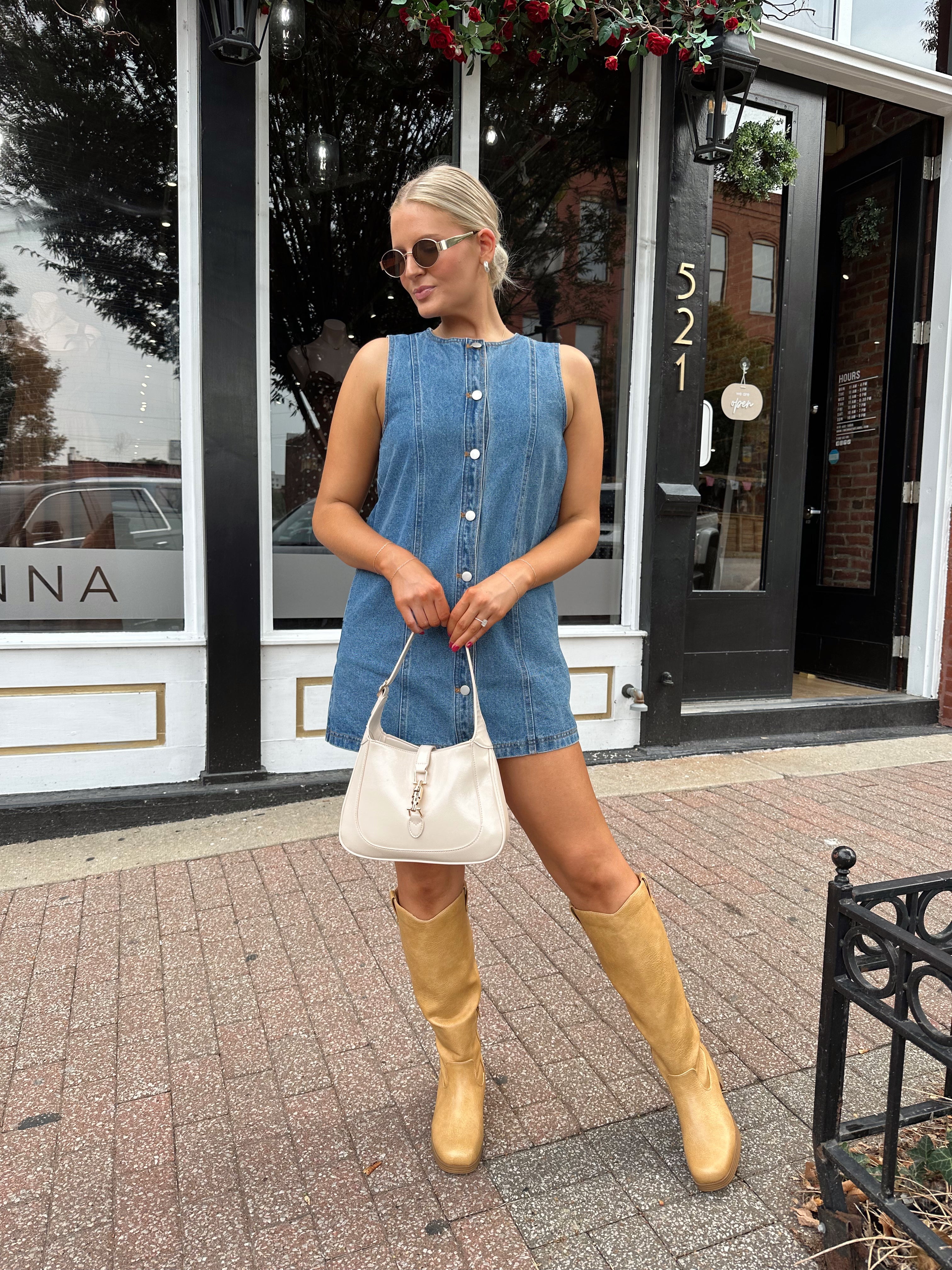 Woman wearing a medium wash denim mini dress with front button closure. 