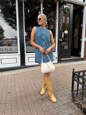 Woman wearing a medium wash denim mini dress with front button closure. 
