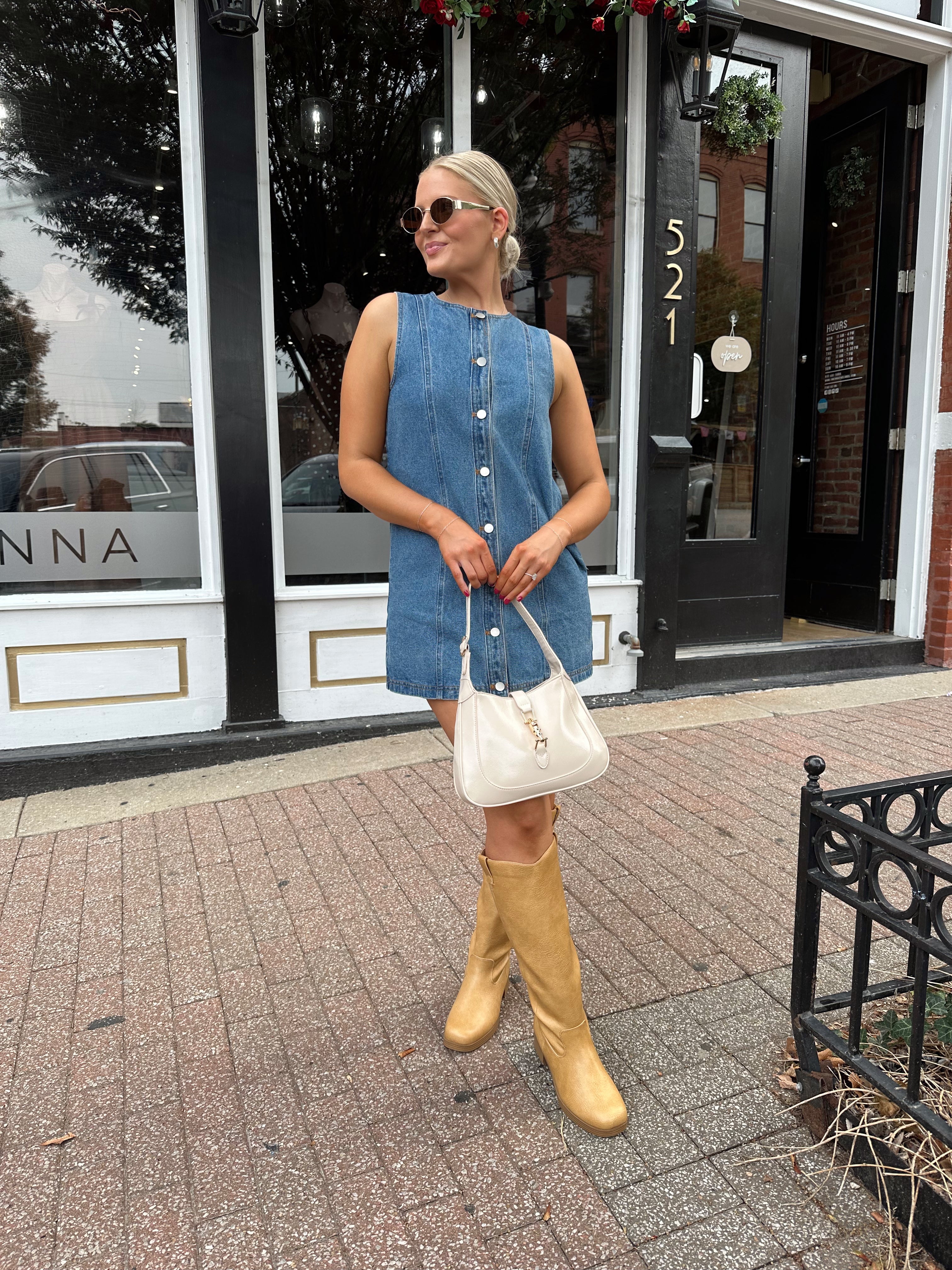 Woman wearing a medium wash denim mini dress with front button closure. 