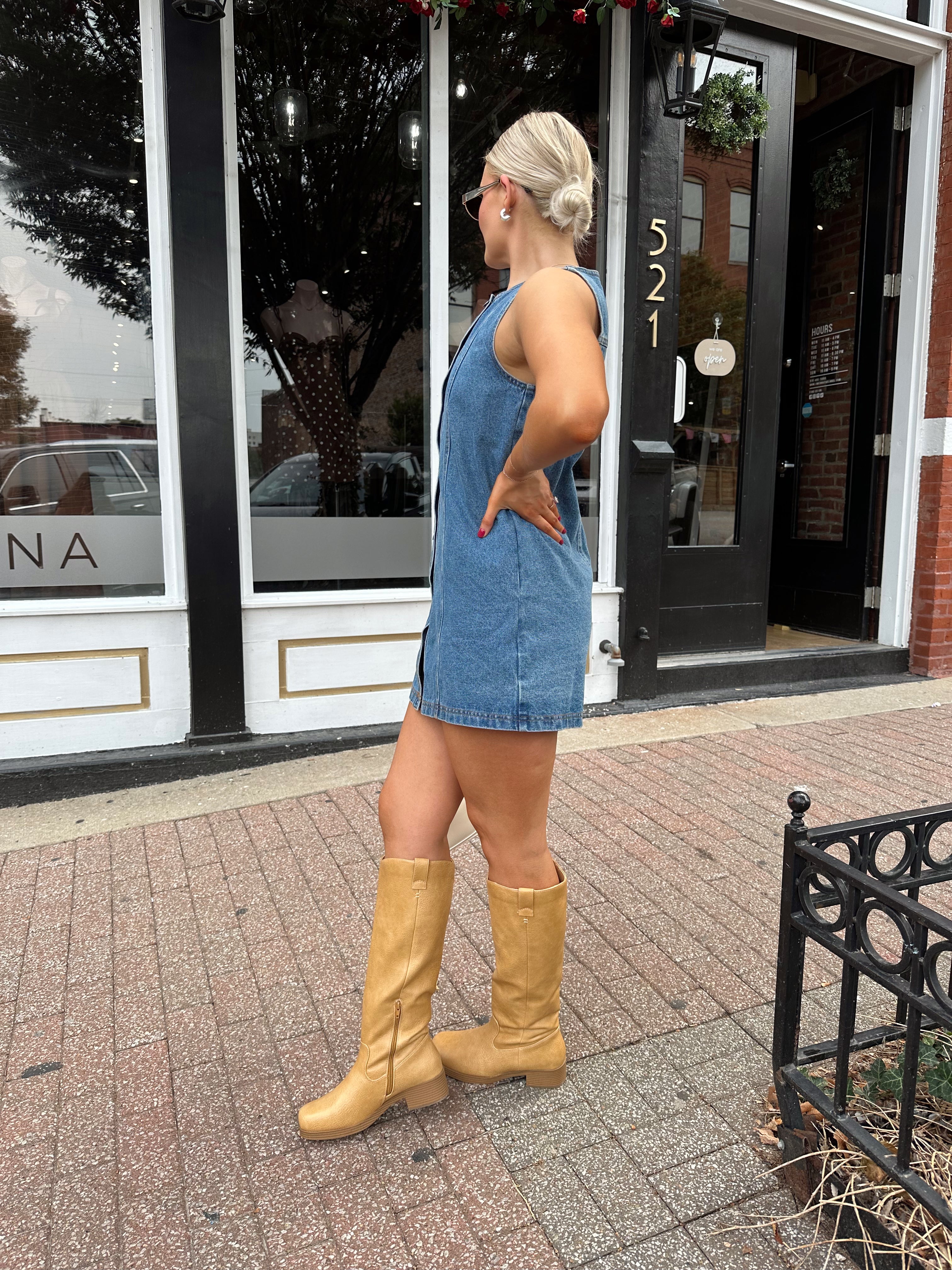 Woman wearing a medium wash denim mini dress with front button closure. 