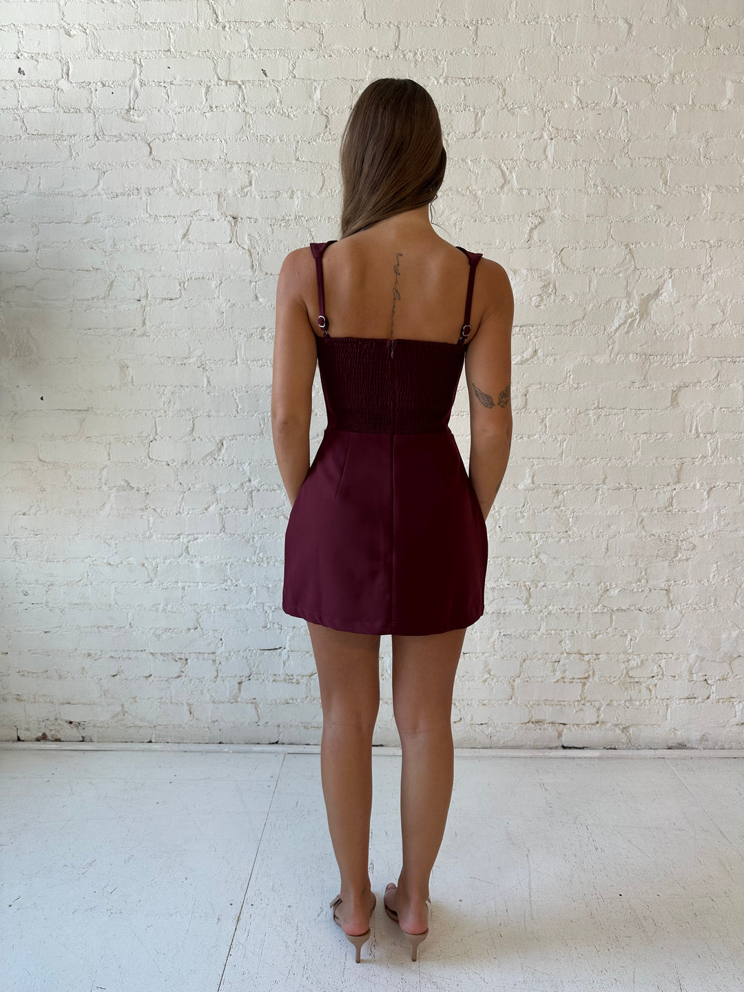 Woman wearing burgundy tailored mini dress with built in shorts. 