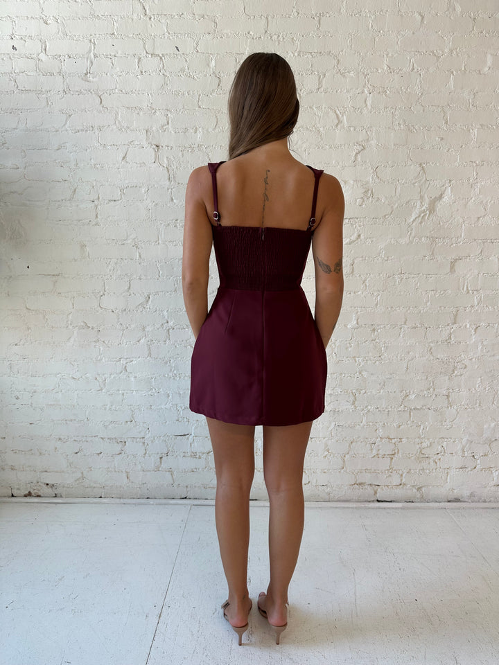Woman wearing burgundy tailored mini dress with built in shorts. 