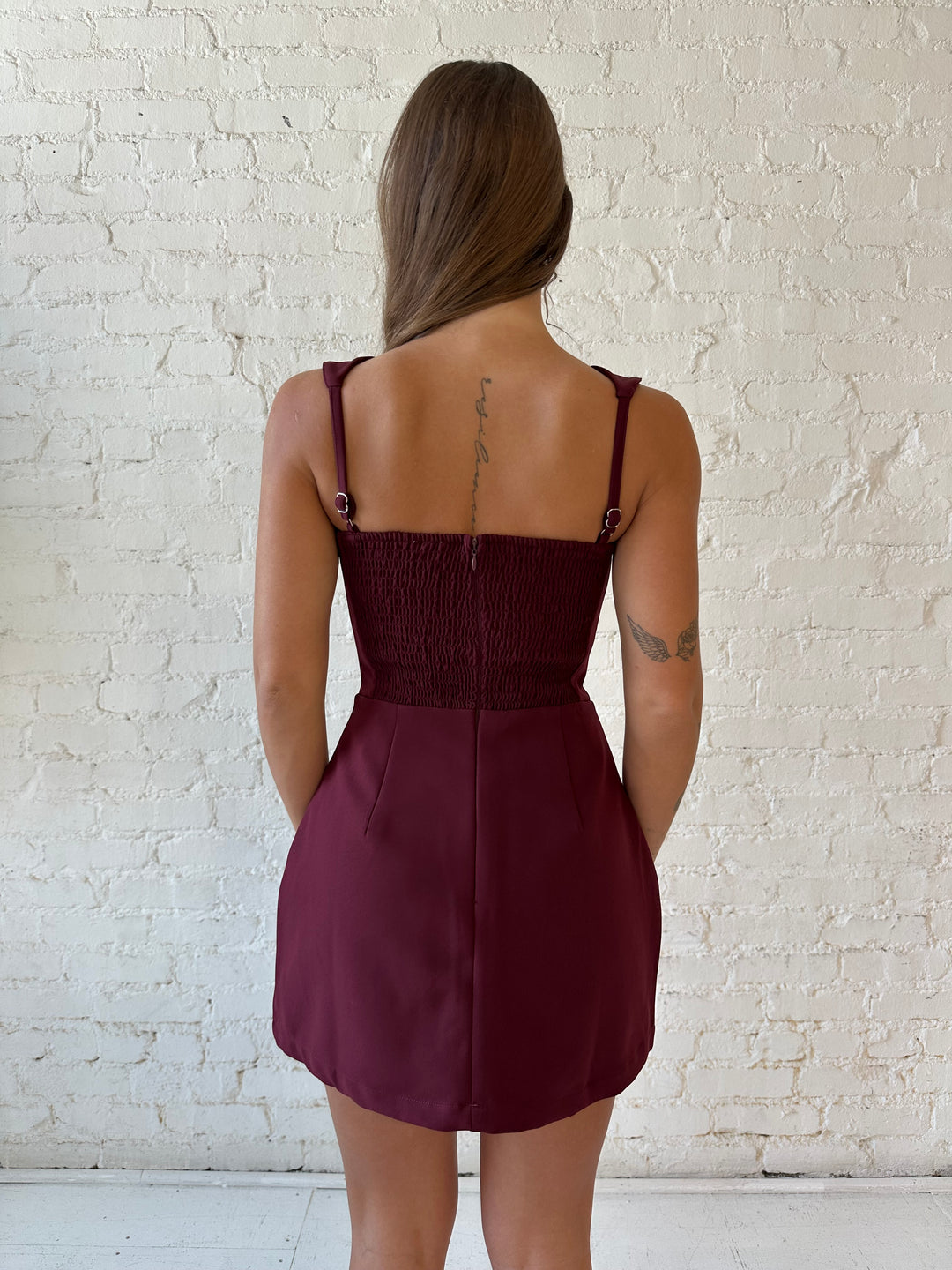 Woman wearing burgundy tailored mini dress with built in shorts. 