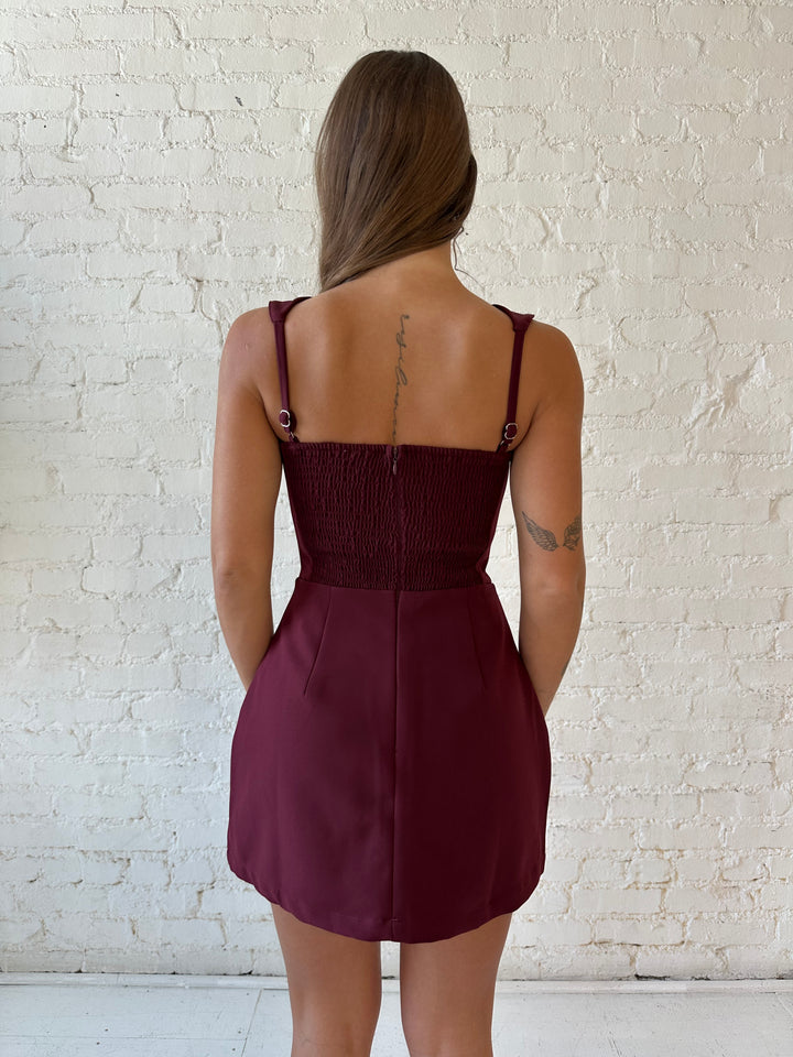 Woman wearing burgundy tailored mini dress with built in shorts. 