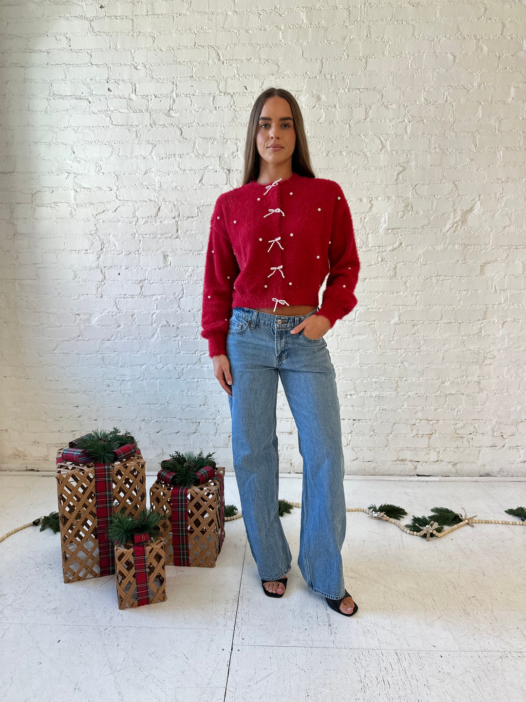 Woman wearing bright red knit cardigan with pearl accents, and pearl bow button closure. 