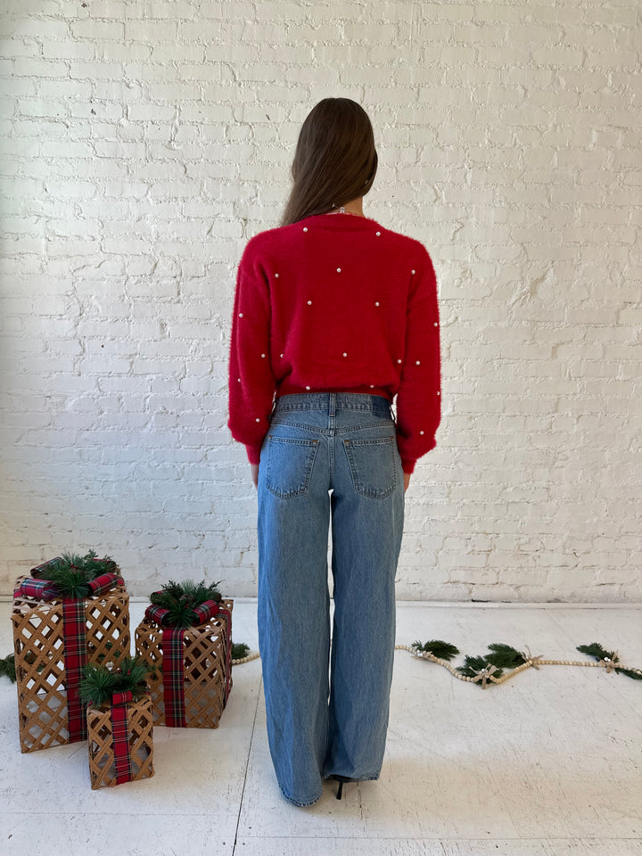 Woman wearing bright red knit cardigan with pearl accents, and pearl bow button closure. 