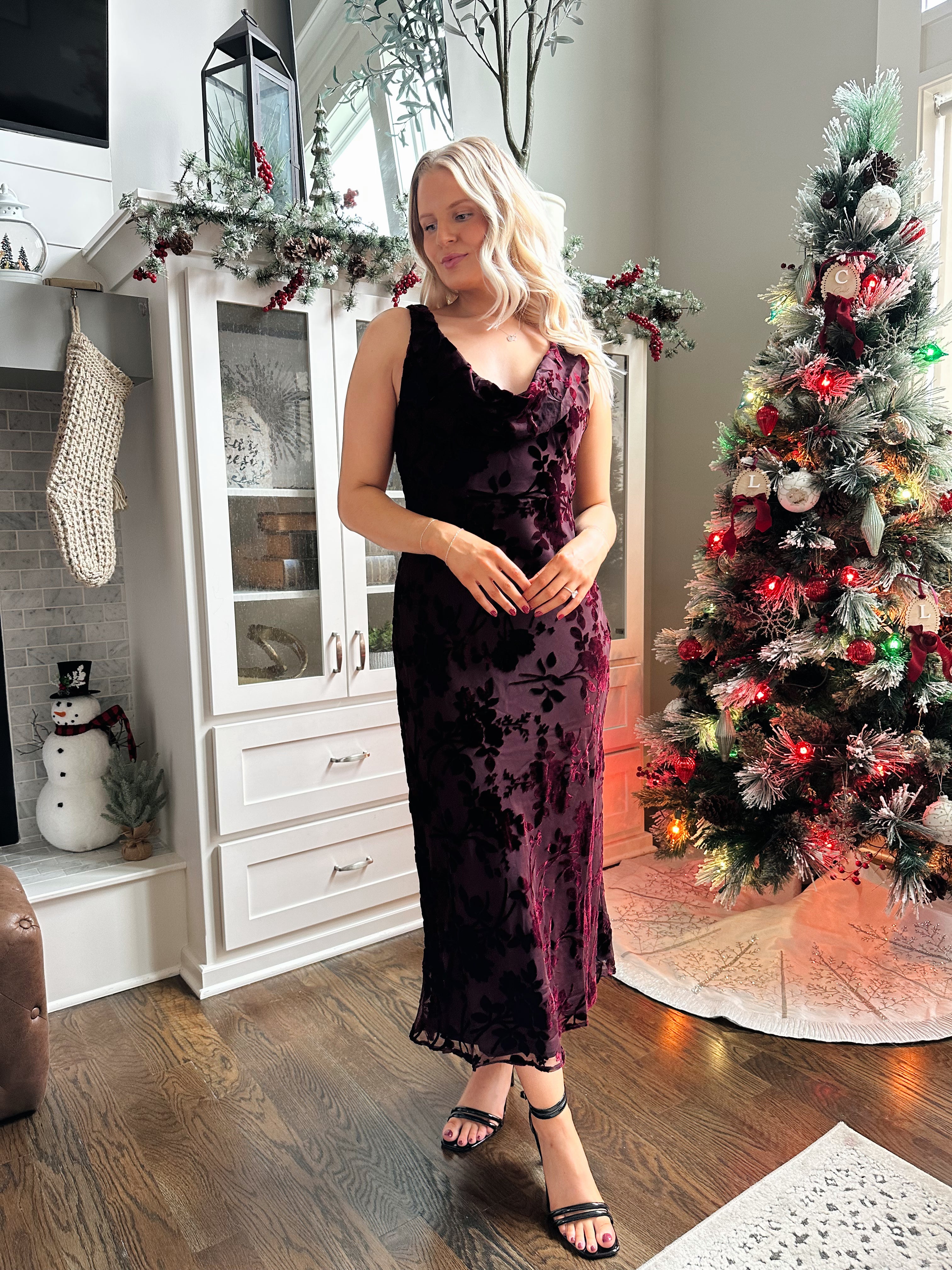 Woman wearing burgundy floral velvet midi dress with cowl neckline. 