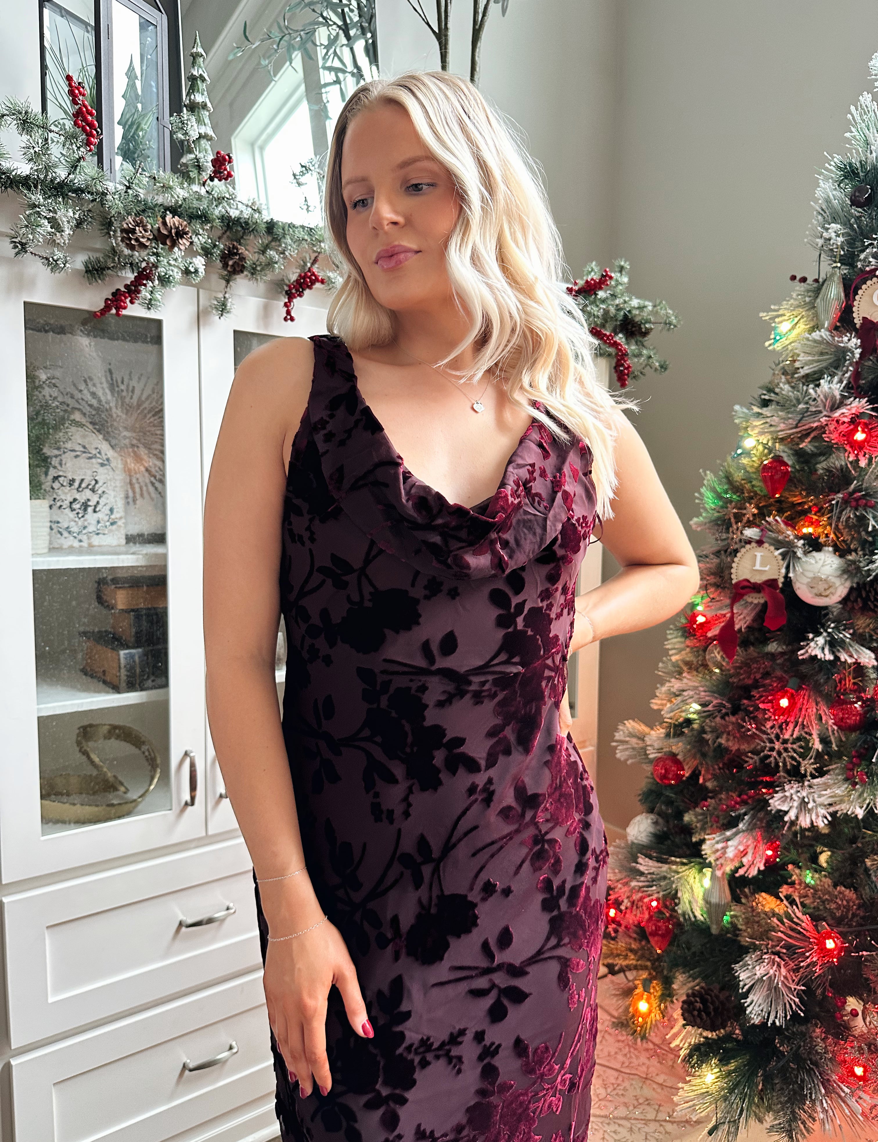 Woman wearing burgundy floral velvet midi dress with cowl neckline. 