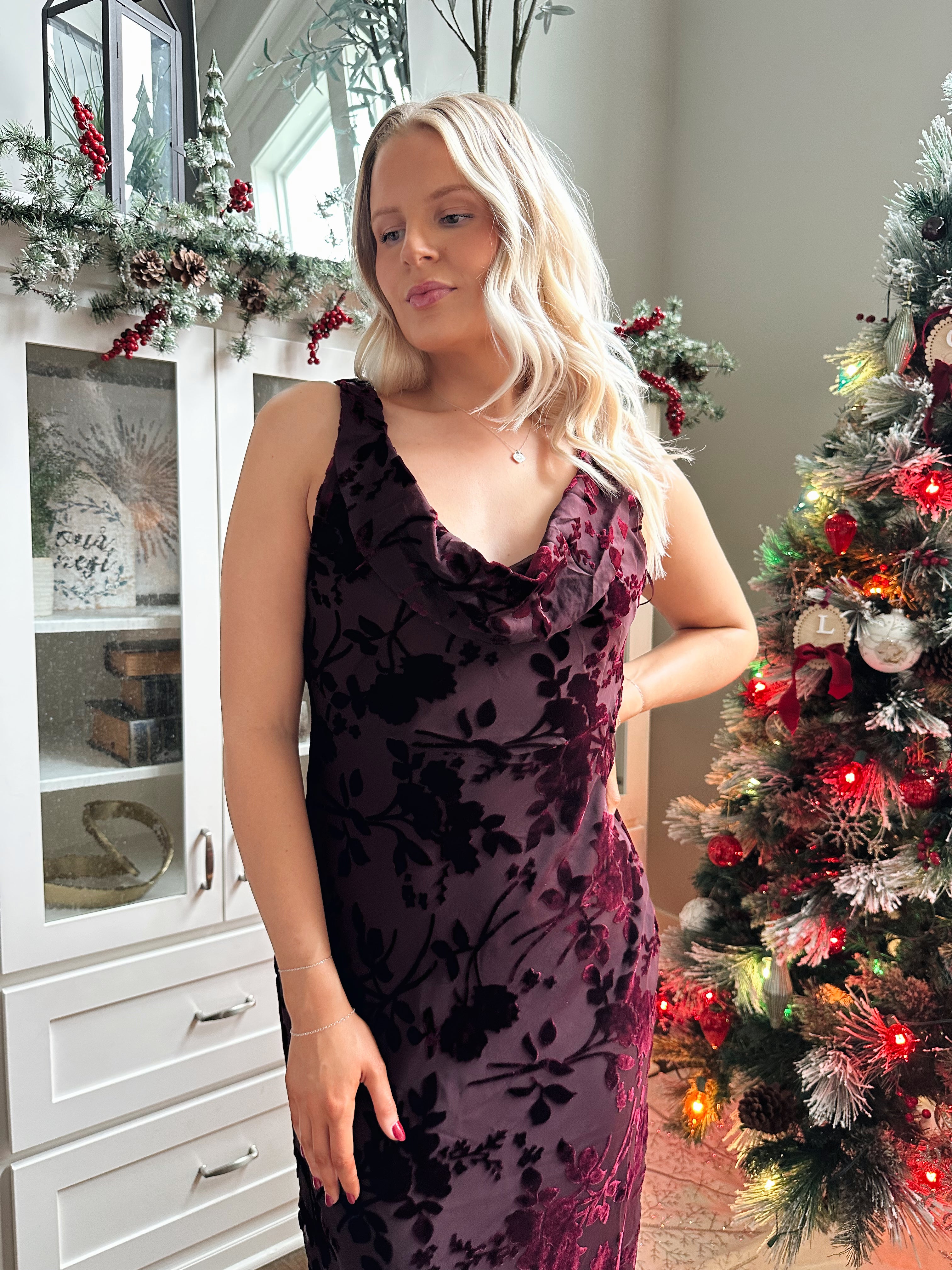 Woman wearing burgundy floral velvet midi dress with cowl neckline. 