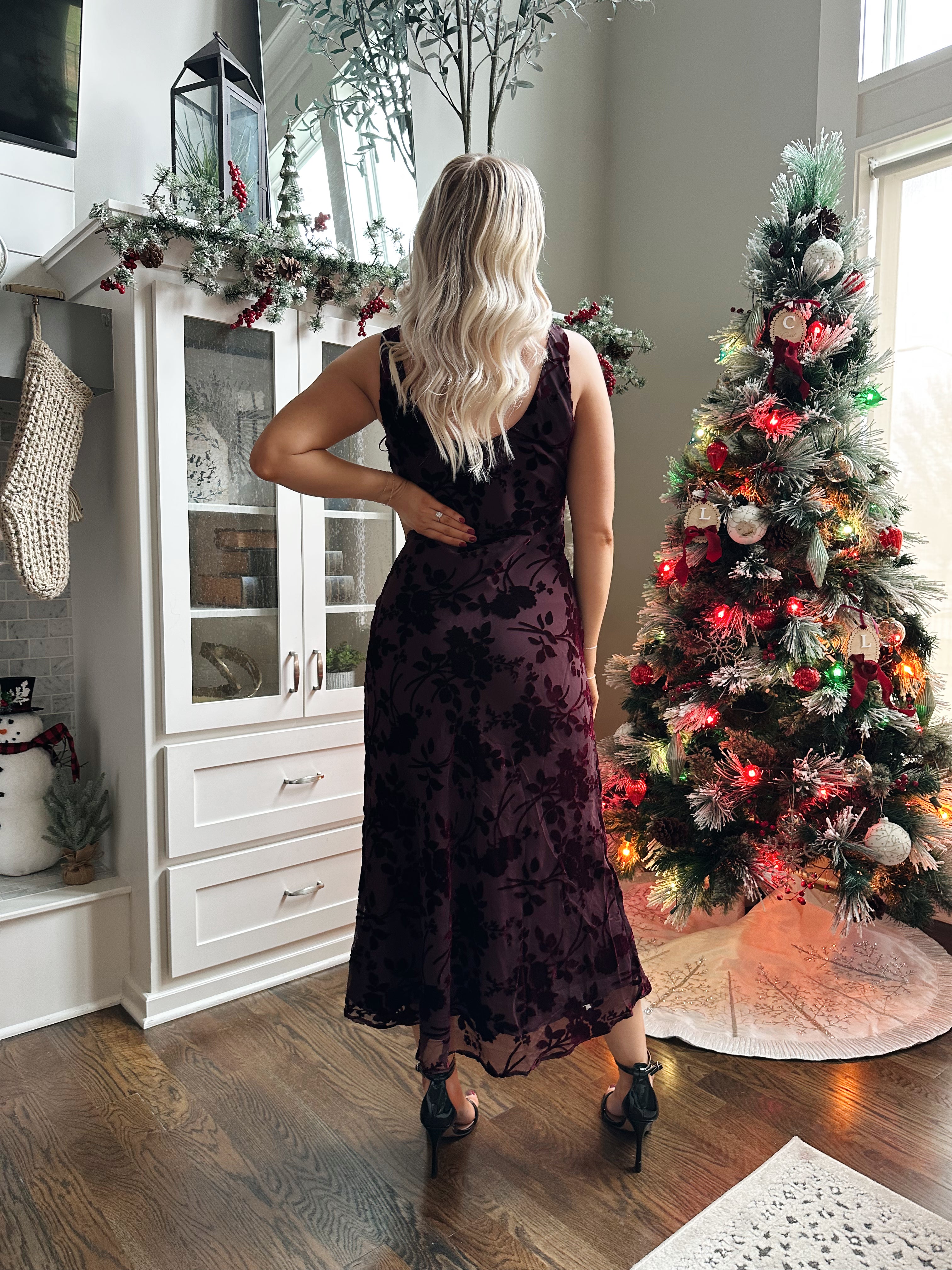 Woman wearing burgundy floral velvet midi dress with cowl neckline. 