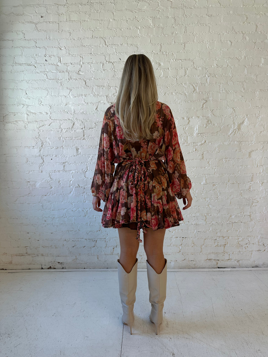 Woman wearing pink and brown floral long sleeve flouncey mini dress with braided waist tie. 