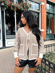 Woman wearing taupe tie front cardigan with functional pockets and contrast trim detail.