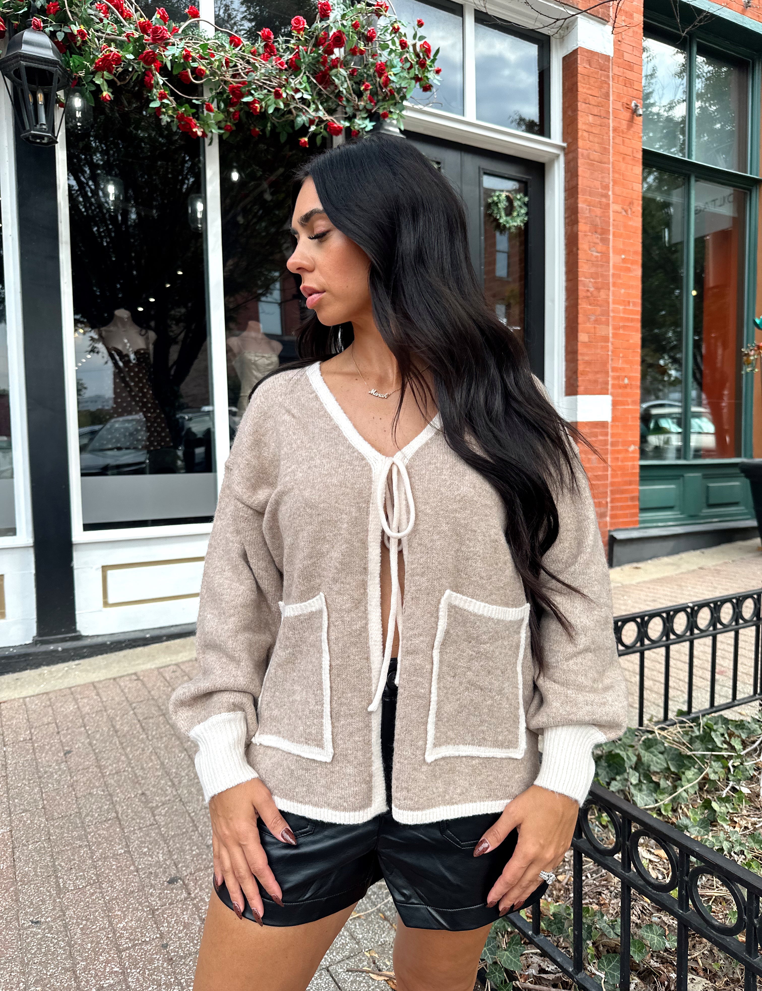 Woman wearing taupe tie front cardigan with functional pockets and contrast trim detail.
