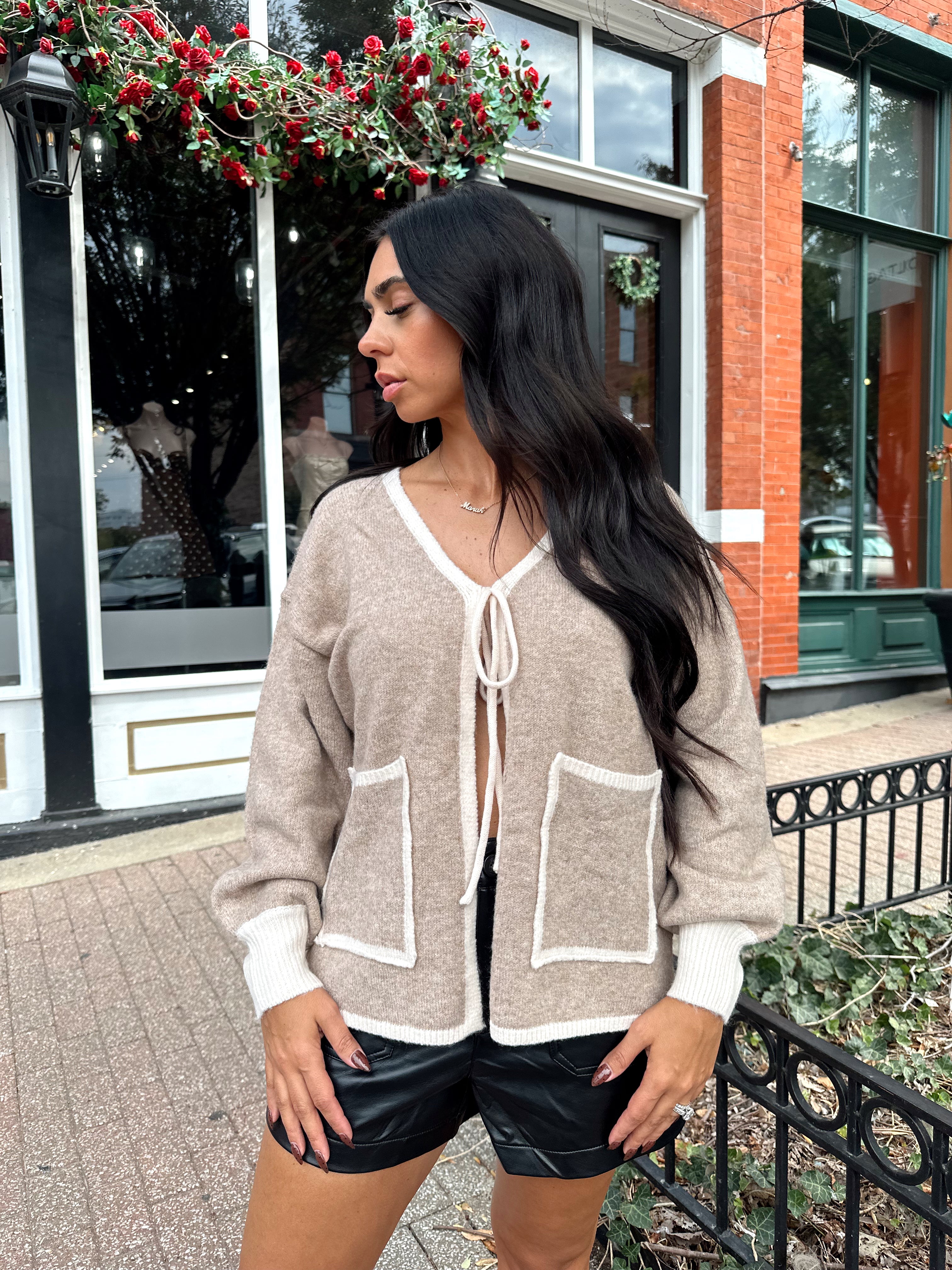 Woman wearing taupe tie front cardigan with functional pockets and contrast trim detail.