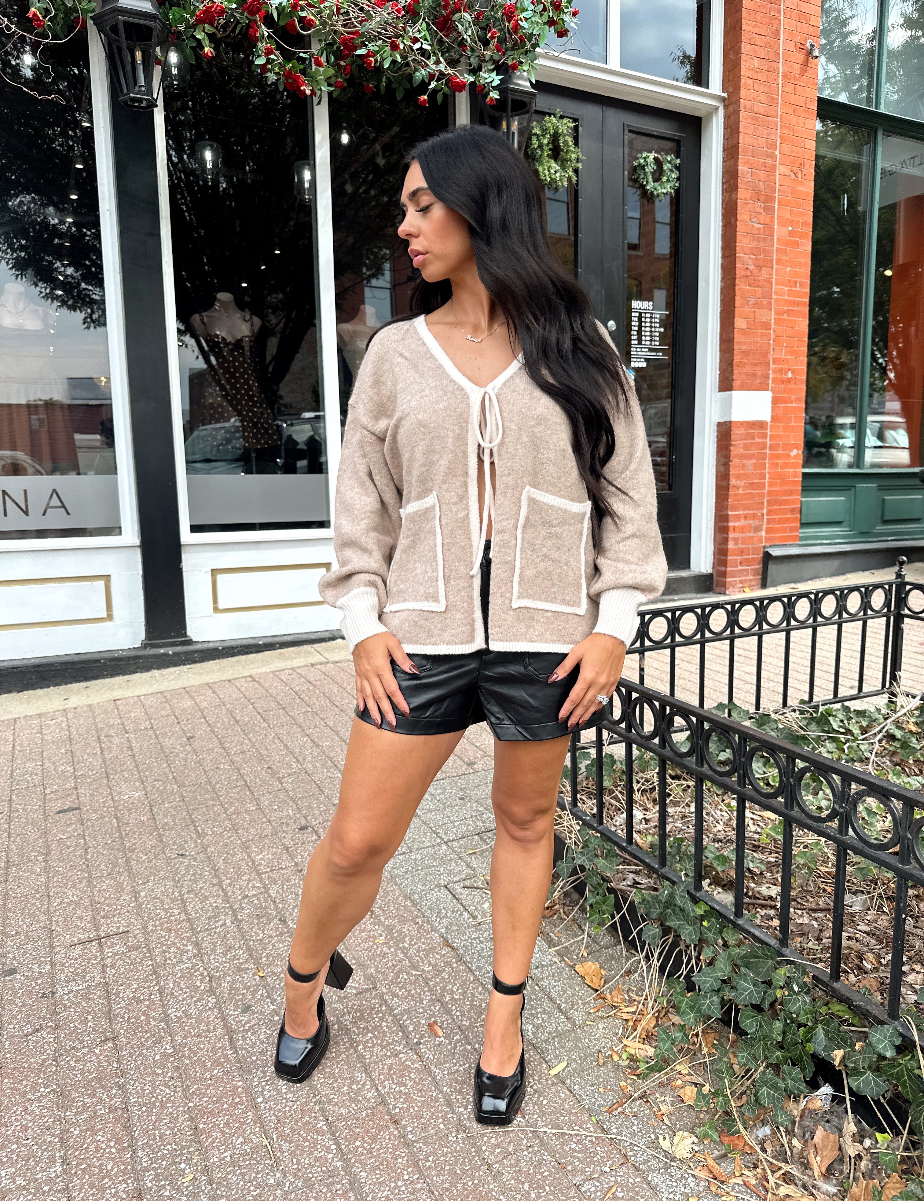 Woman wearing taupe tie front cardigan with functional pockets and contrast trim detail.