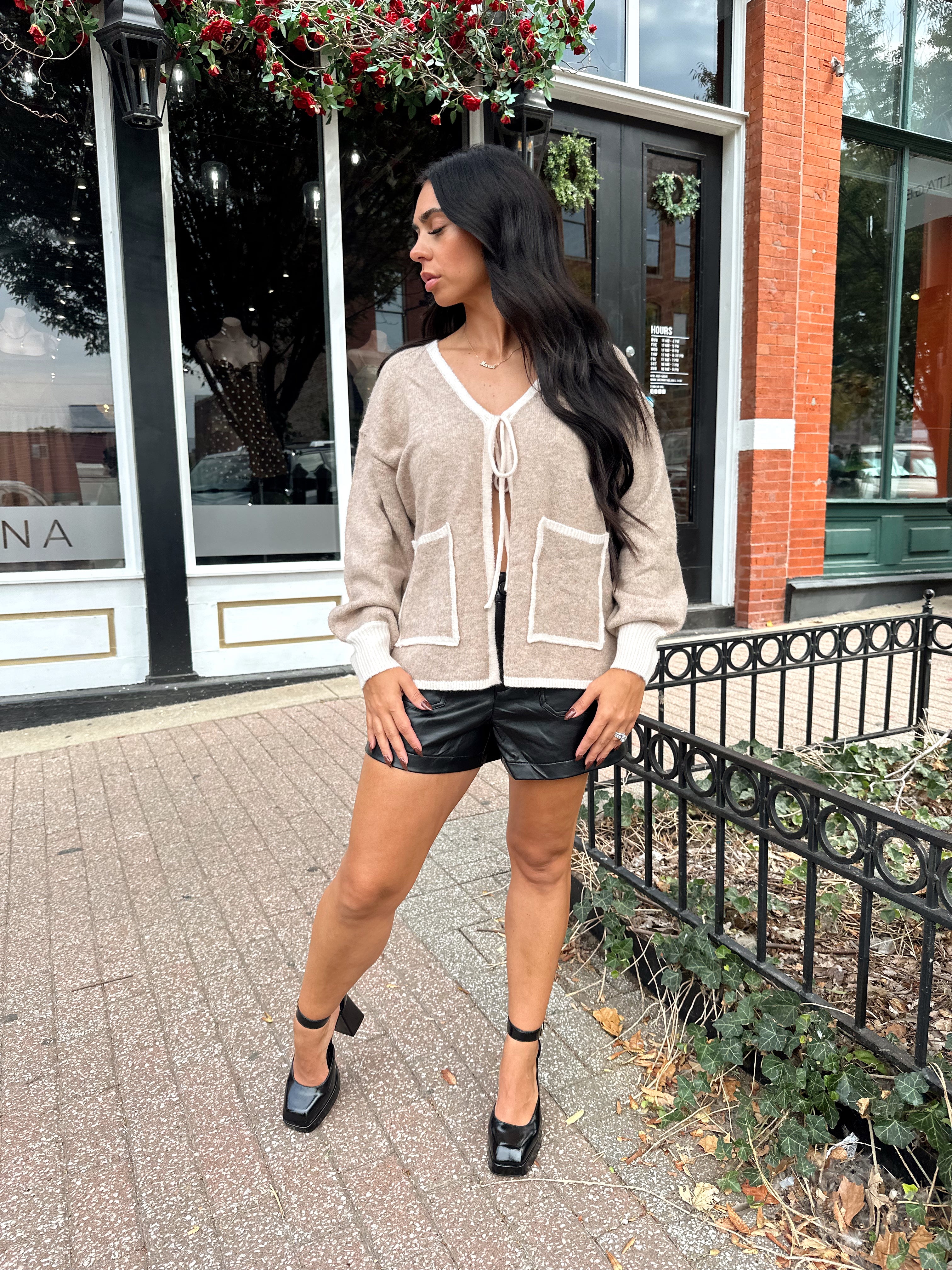 Woman wearing taupe tie front cardigan with functional pockets and contrast trim detail.