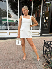 Woman wearing white tailored mini dress with built in shorts and adjustable straps.