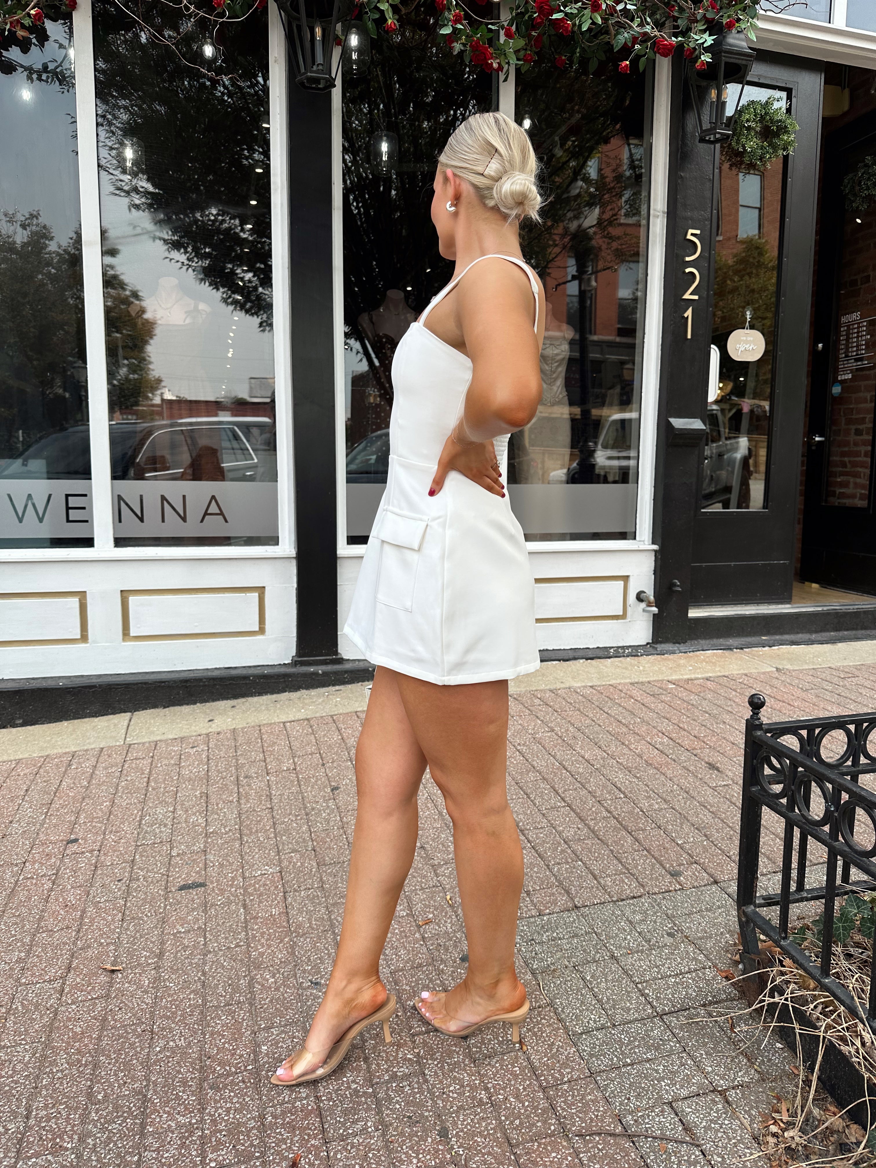 Woman wearing white tailored mini dress with built in shorts and adjustable straps.