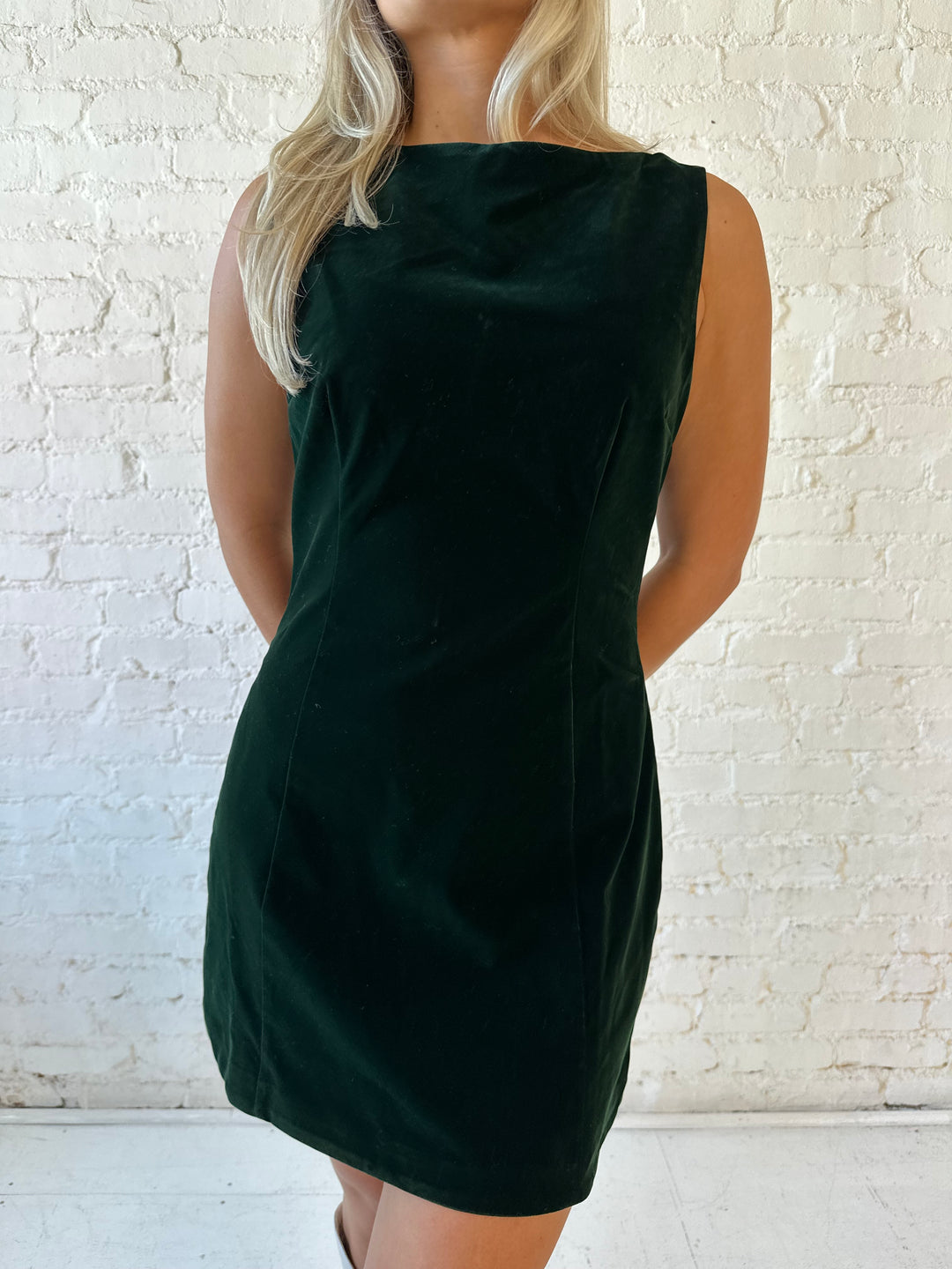 Woman wearing dark green velvet A-line mini dress with high neckline, and v-back. 