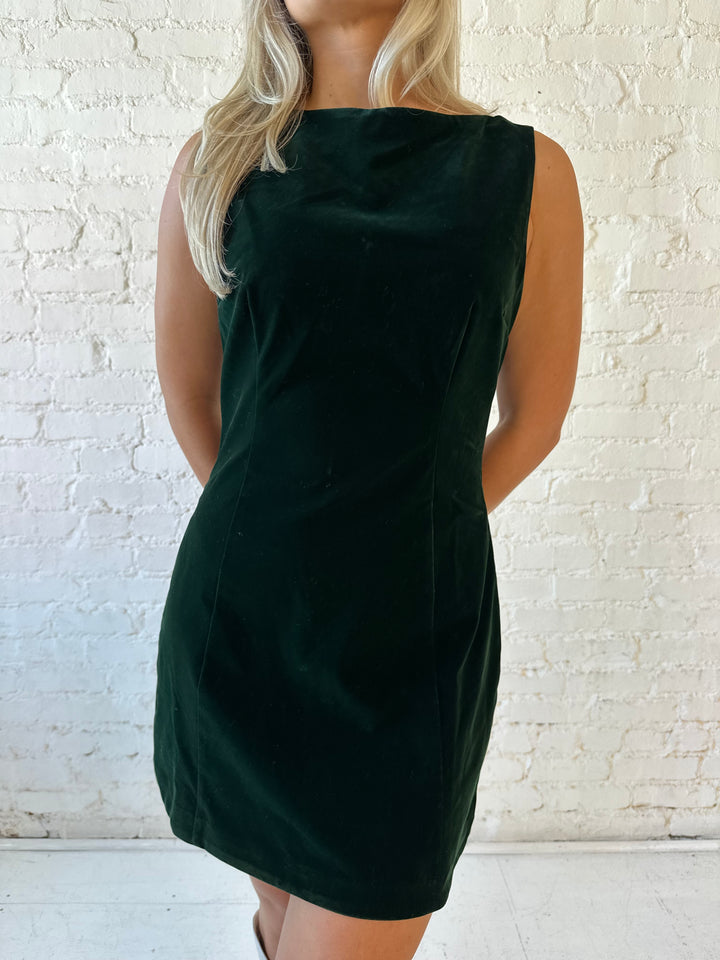 Woman wearing dark green velvet A-line mini dress with high neckline, and v-back. 
