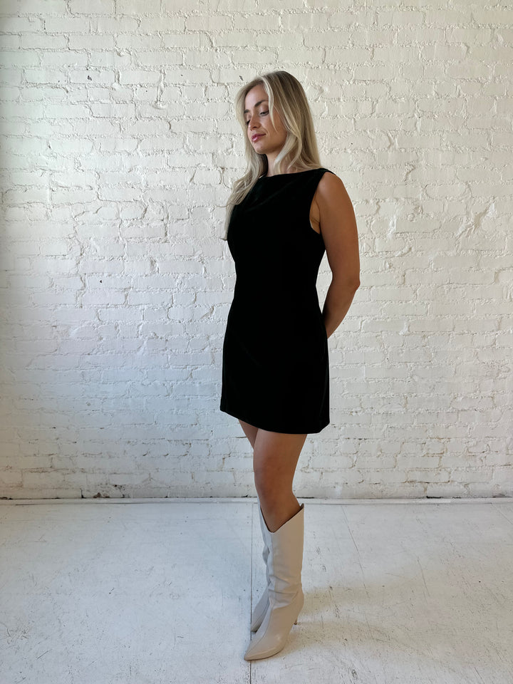 Woman wearing dark green velvet A-line mini dress with high neckline, and v-back. 