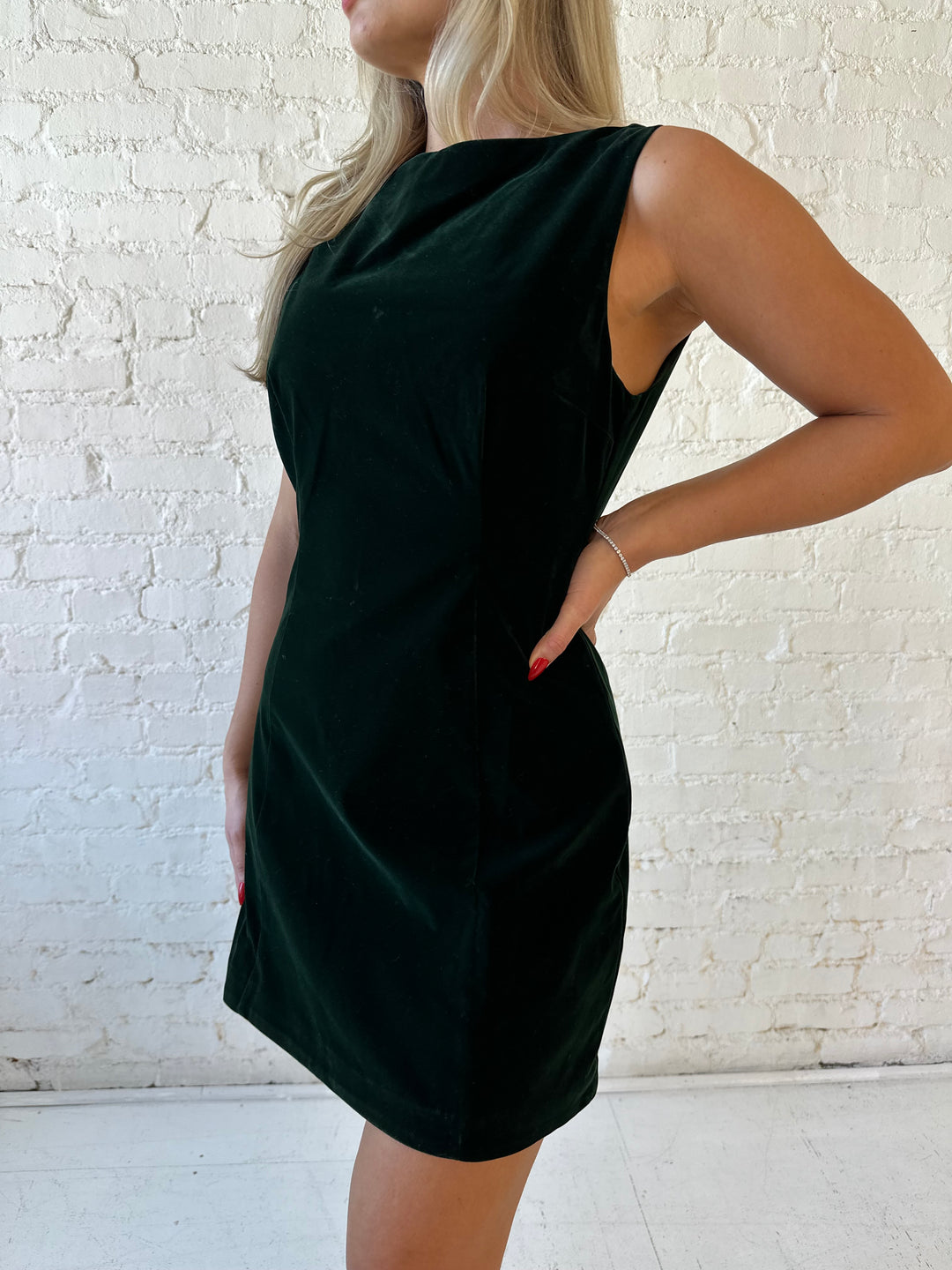 Woman wearing dark green velvet A-line mini dress with high neckline, and v-back. 